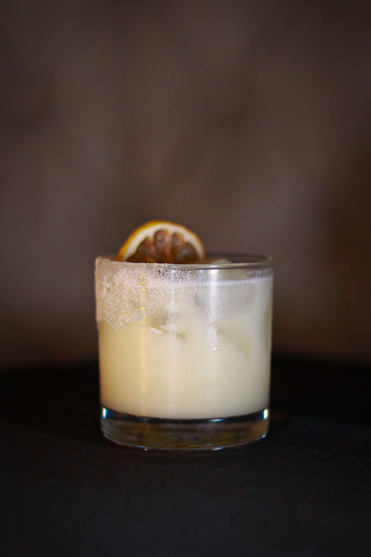 Creamy cocktail with frothy top served in a short glass with dark background.