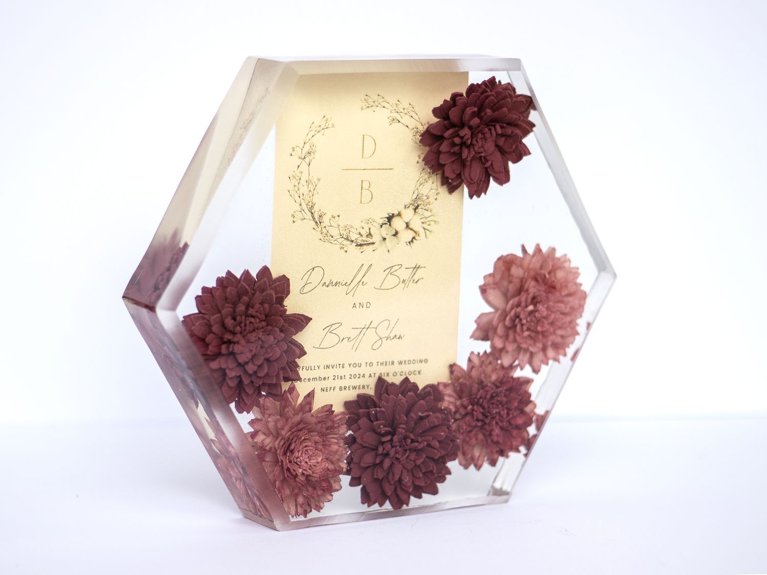 Hexagonal resin keepsake with dried burgundy flowers and gold wedding invitation encapsulated inside.