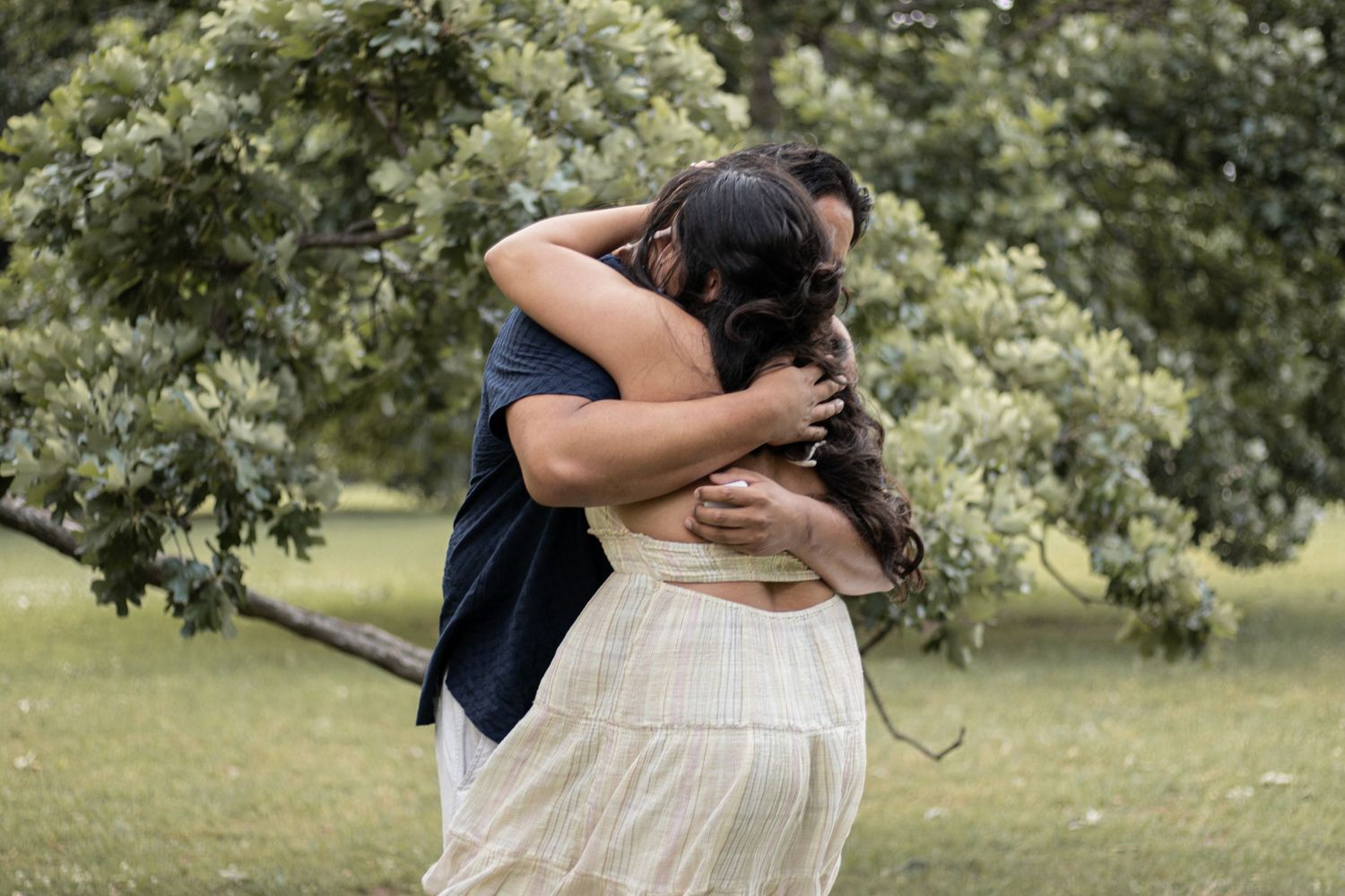 Couple sharing a joyful embrace outdoors after a marriage proposal in a lush green park.