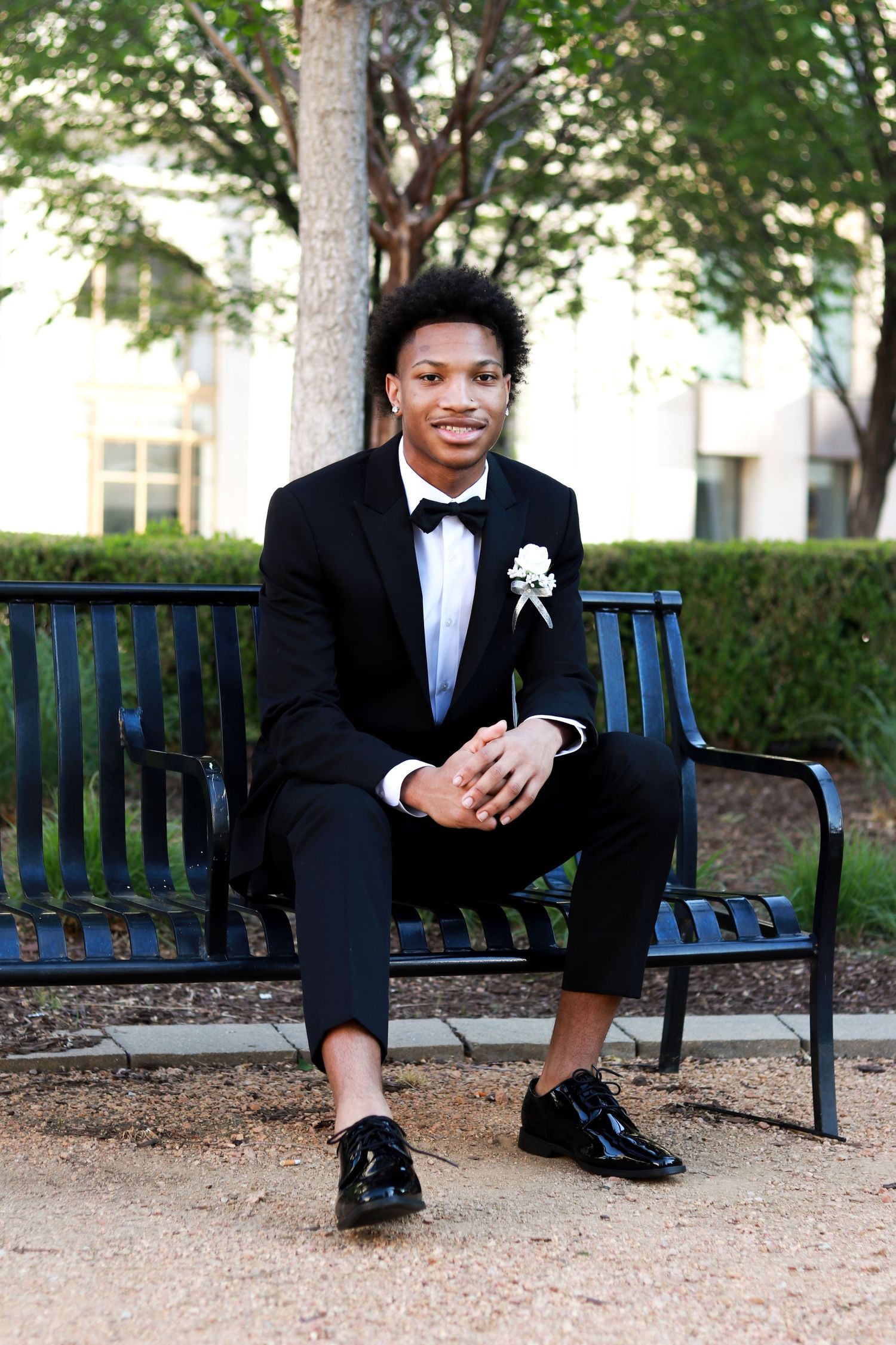 Four stylish prom portraits show someone in a black tuxedo and bowtie sitting on a bench in a garden setting.