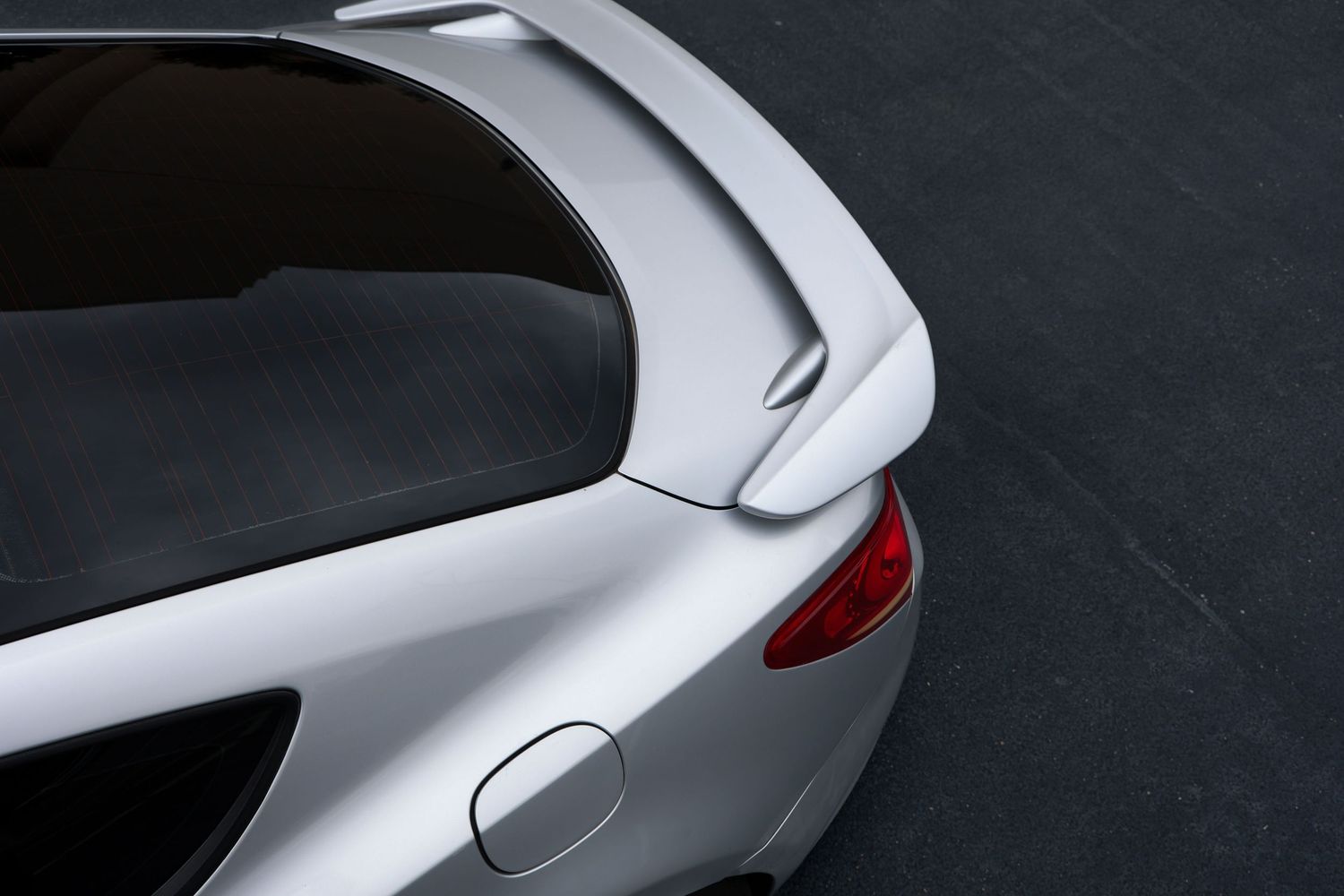Close-up of a silver sports car rear spoiler and tail light on a dark asphalt surface.