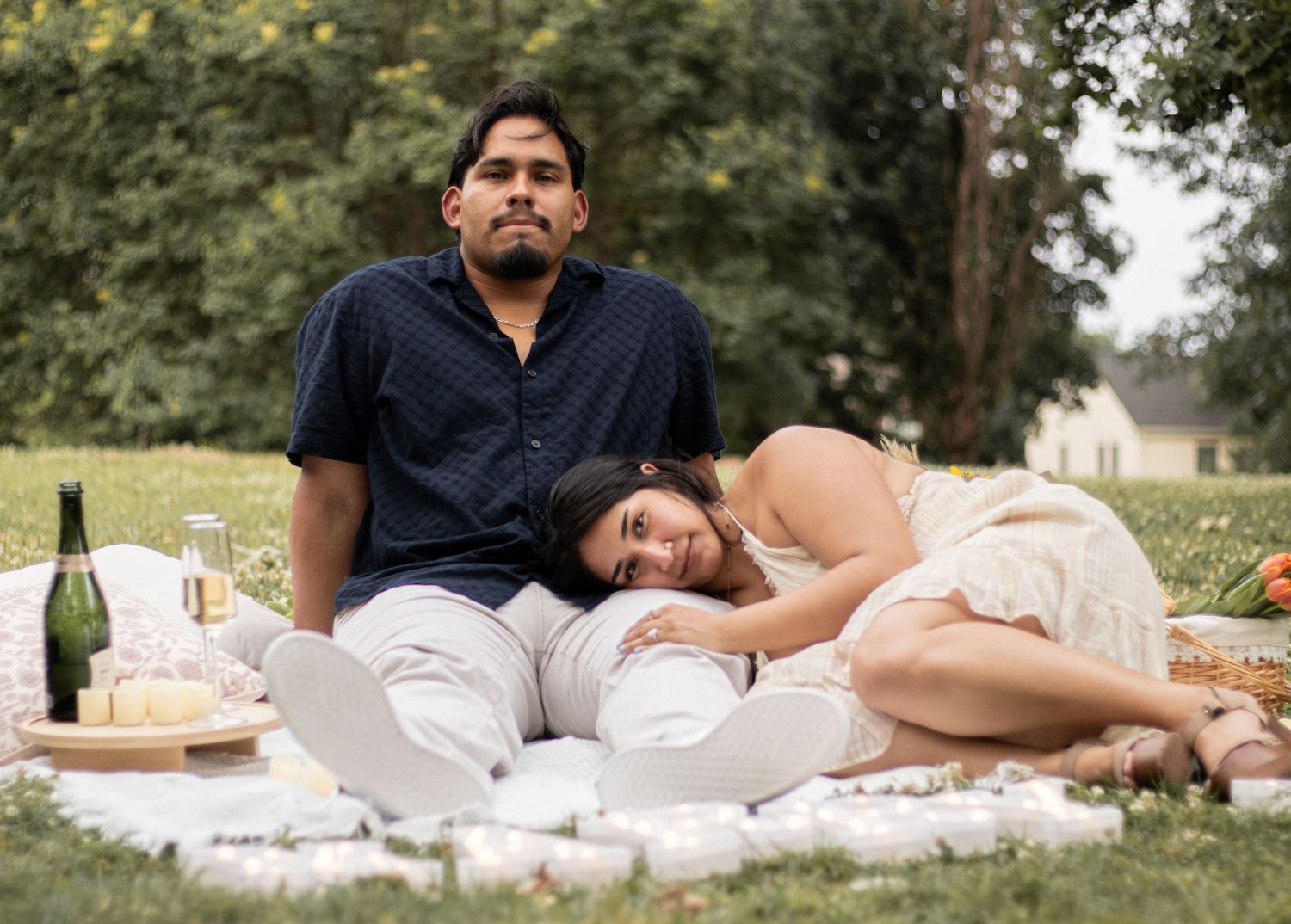 Newly engaged couple relaxing together on a white picnic blanket in a scenic outdoor setting.