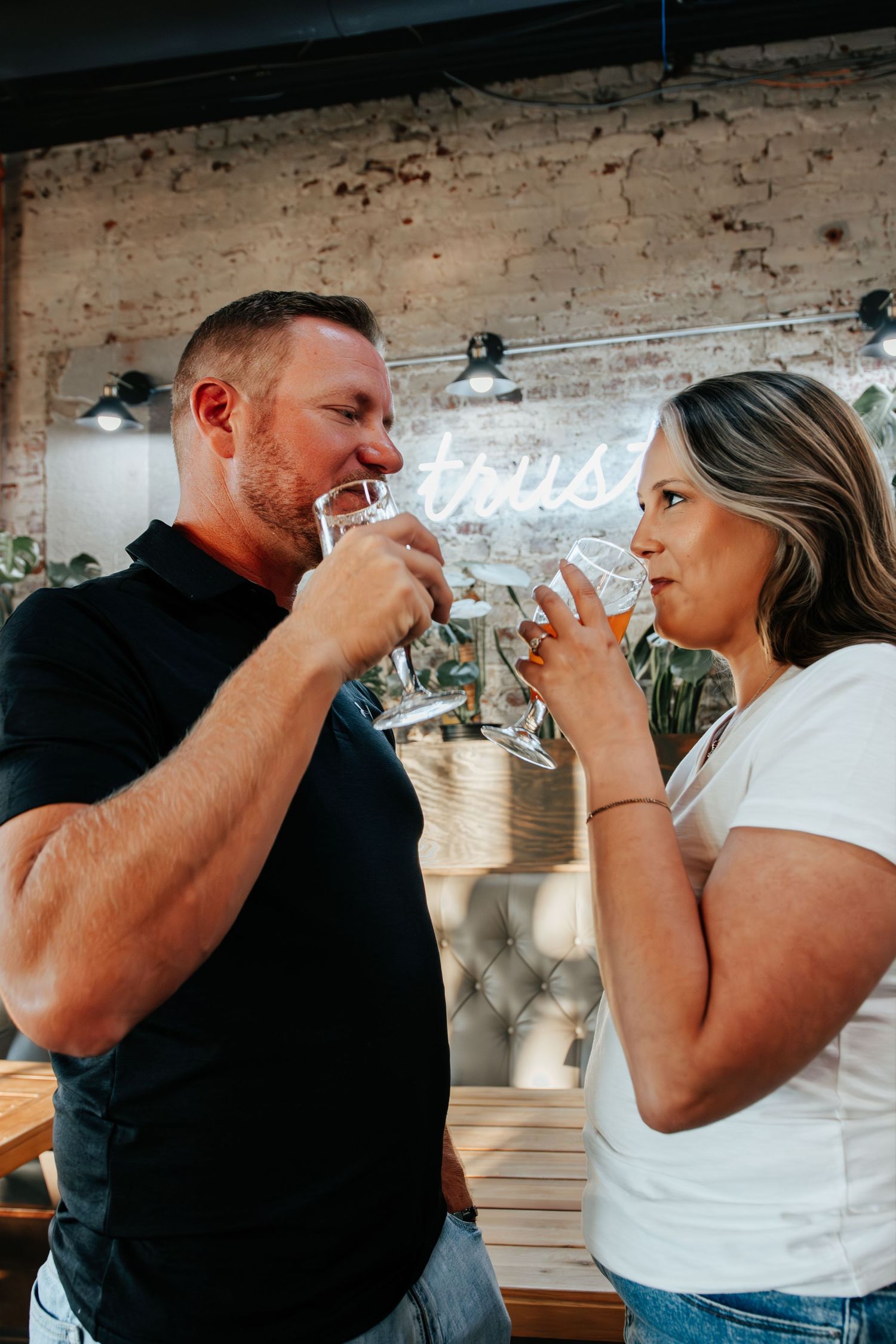 Couple toasting with water glasses at a trendy brick-wall bar with neon sign lighting.