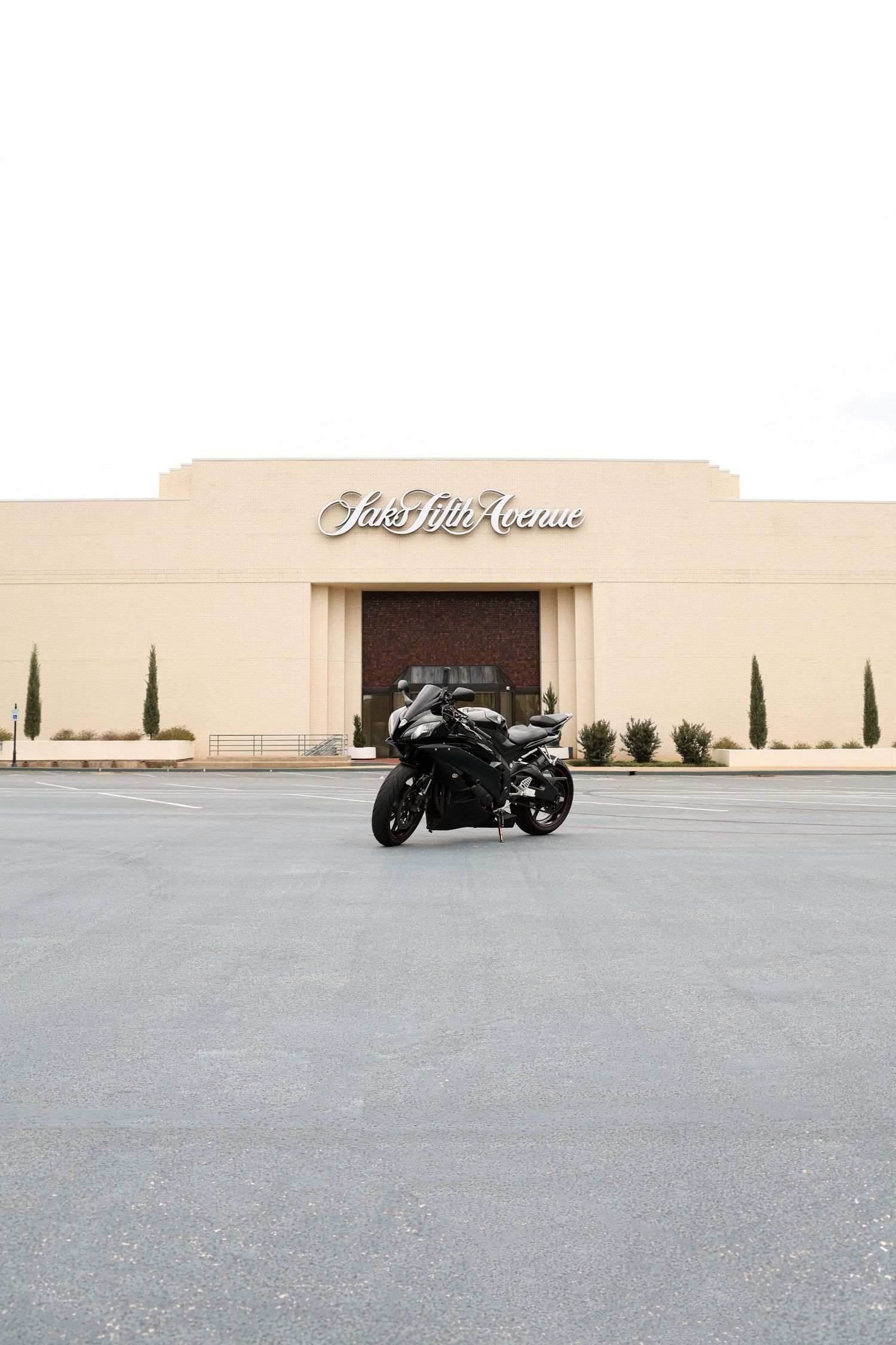 Black sport motorcycle parked in front of Saks Fifth Avenue store in an empty parking lot.