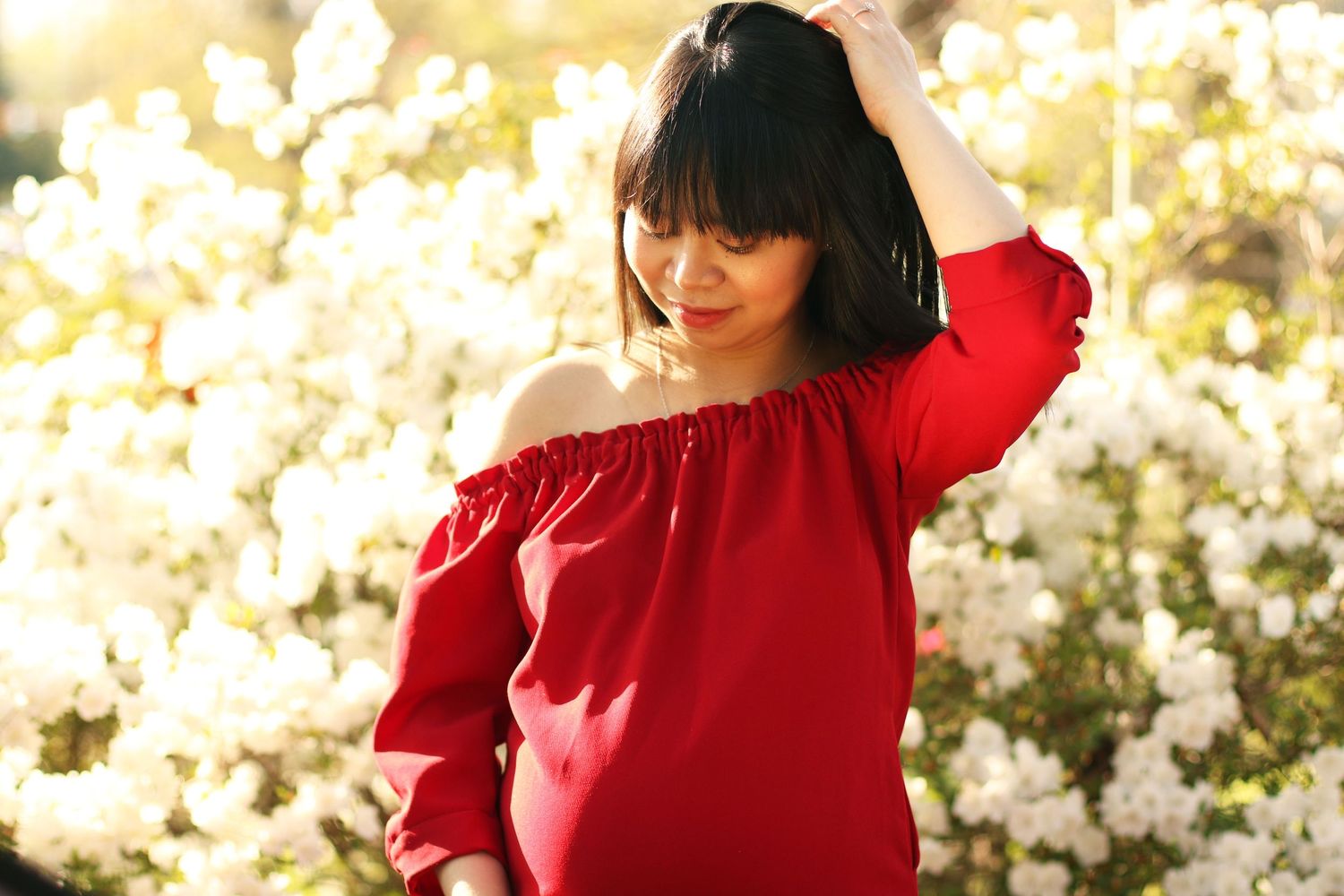 A person in a bright red sweater poses against a backdrop of white cherry blossoms in spring.