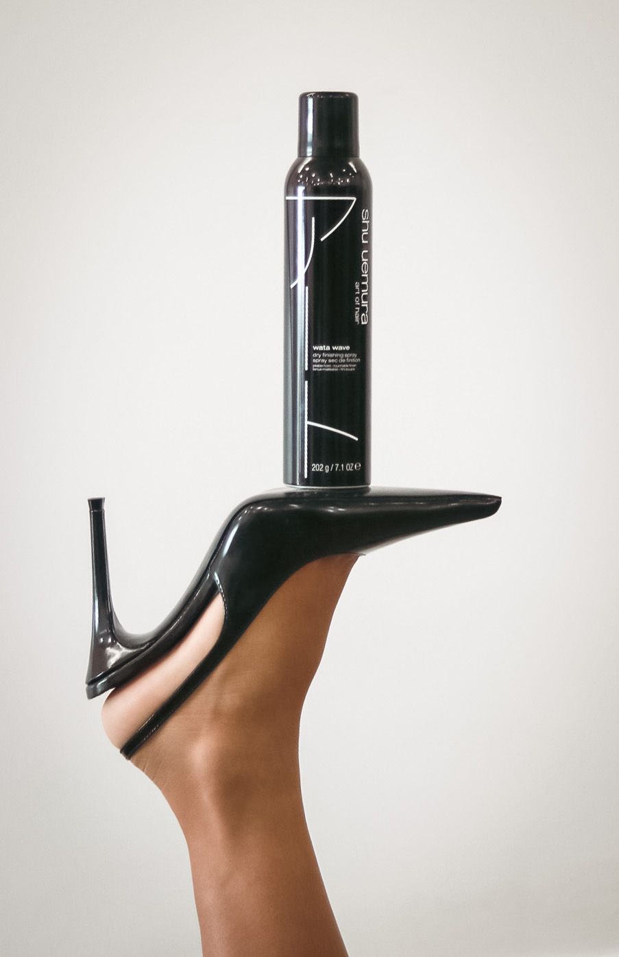 Black perfume bottle balanced on a high heel shoe in a minimalist product photography setup.