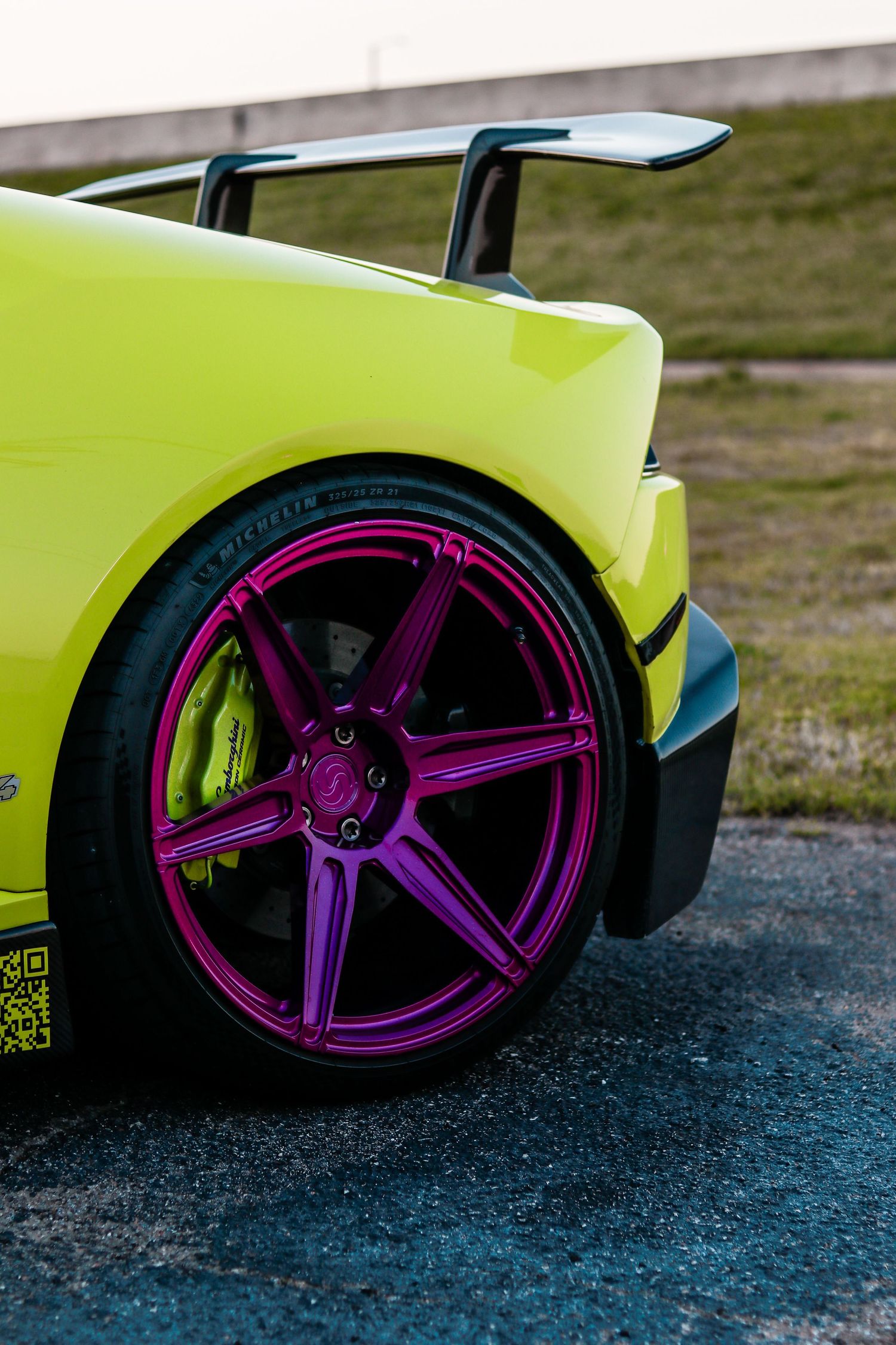 Close-up of a neon yellow Lamborghini's wheel with bright purple custom rims against dark pavement.