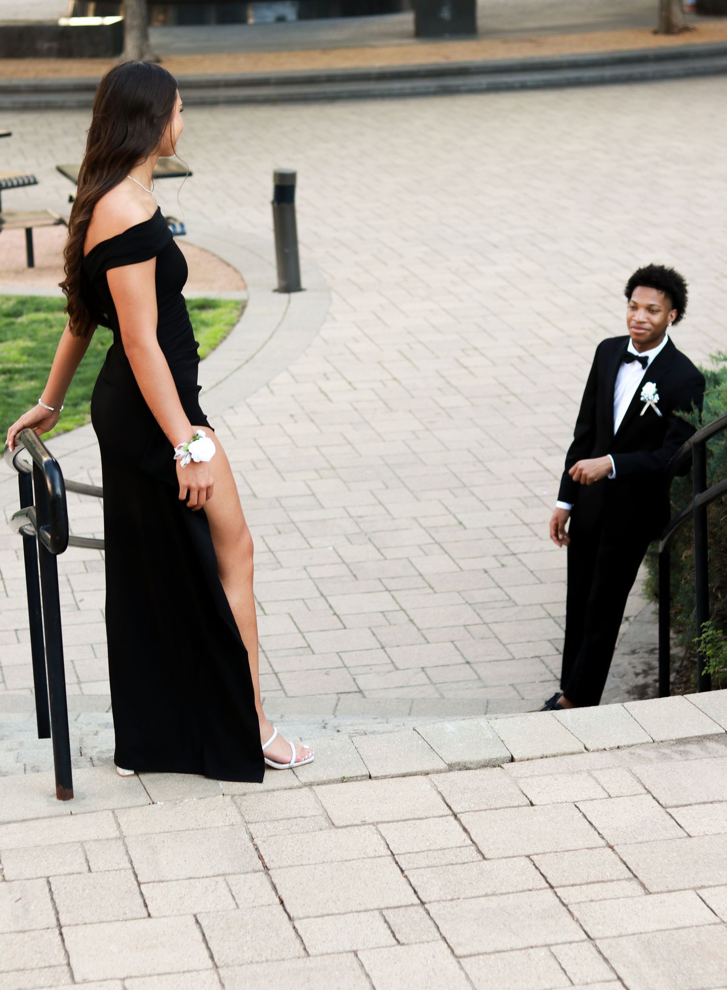 A couple in formal attire poses for creative wedding photos on stone steps in an outdoor setting.