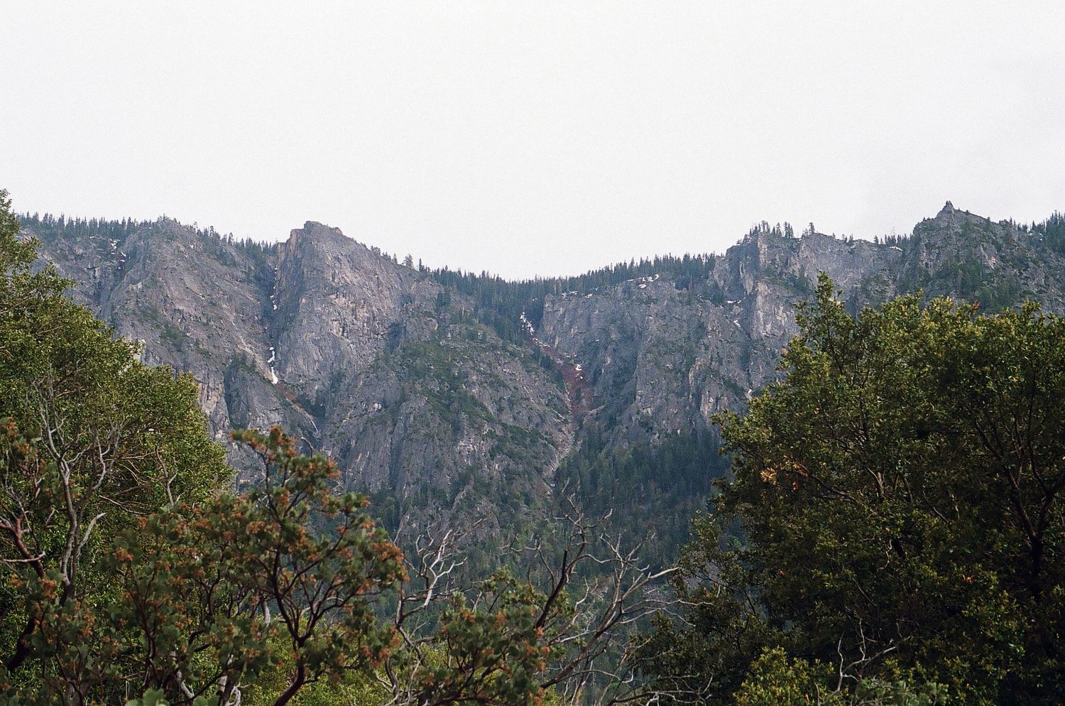 Rugged mountain peaks rise above forested slopes in a natural landscape.