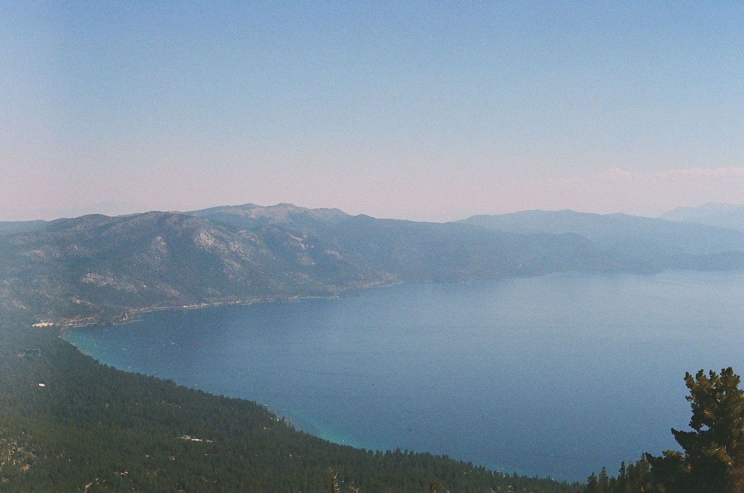 Aerial view of Lake Tahoe surrounded by mountains under clear blue sky.