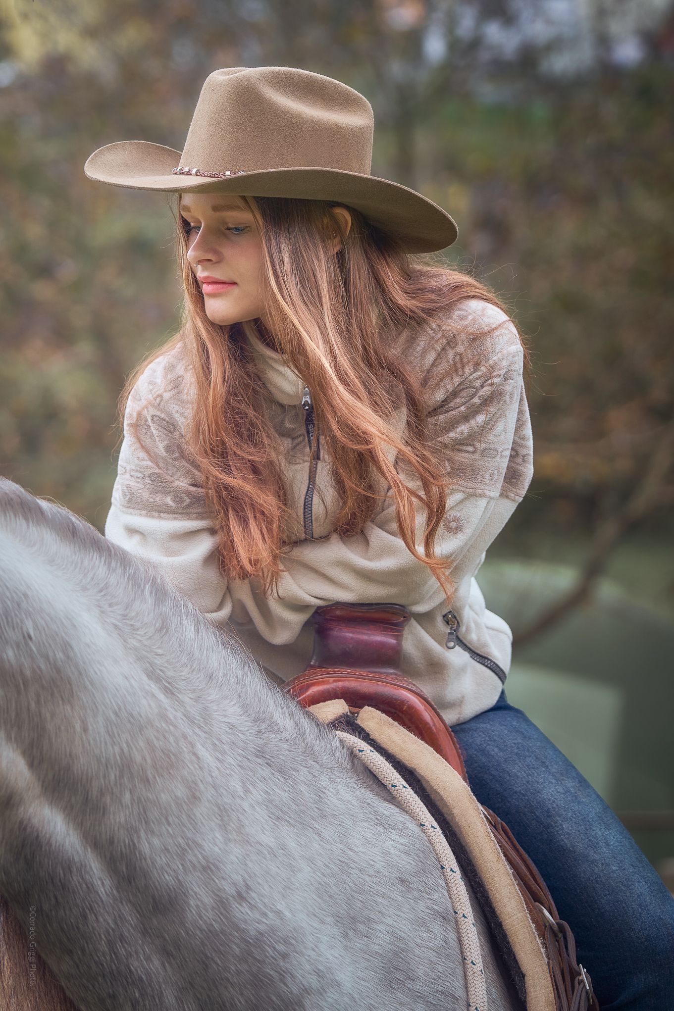 «Ritratto verticale di una giovane amazzone con cappello da cowboy, sguardo sognante, mezzo busto dettagli del cavallo finimenti e sella