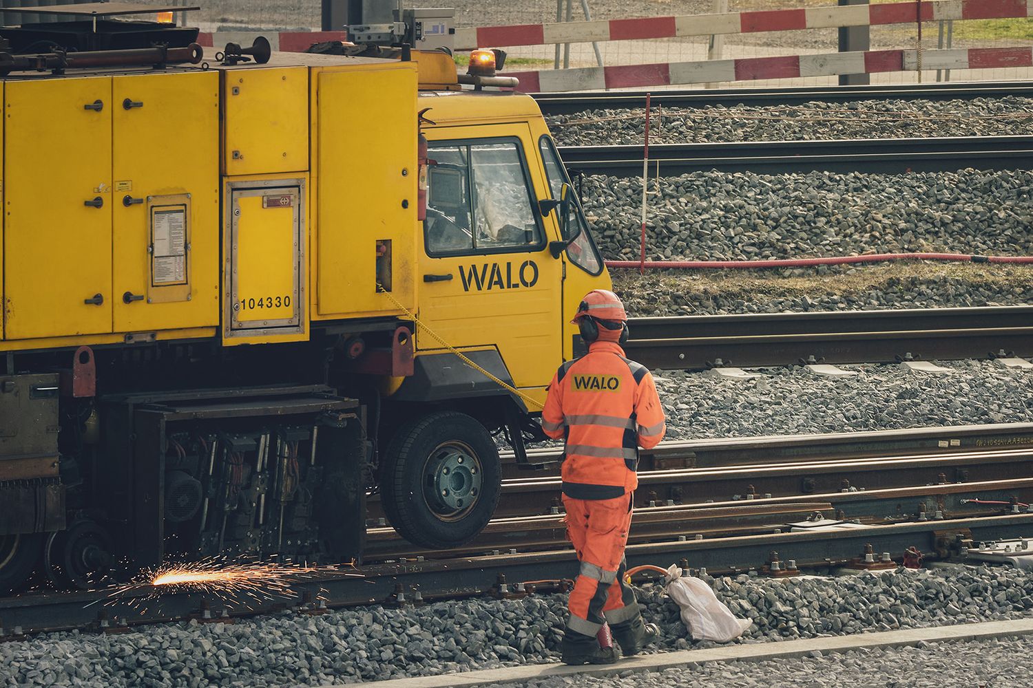 Operatore e mezzo tecnico WALO durante manutenzione sui binari nel cantiere ferroviario con scintille di lavorazione.