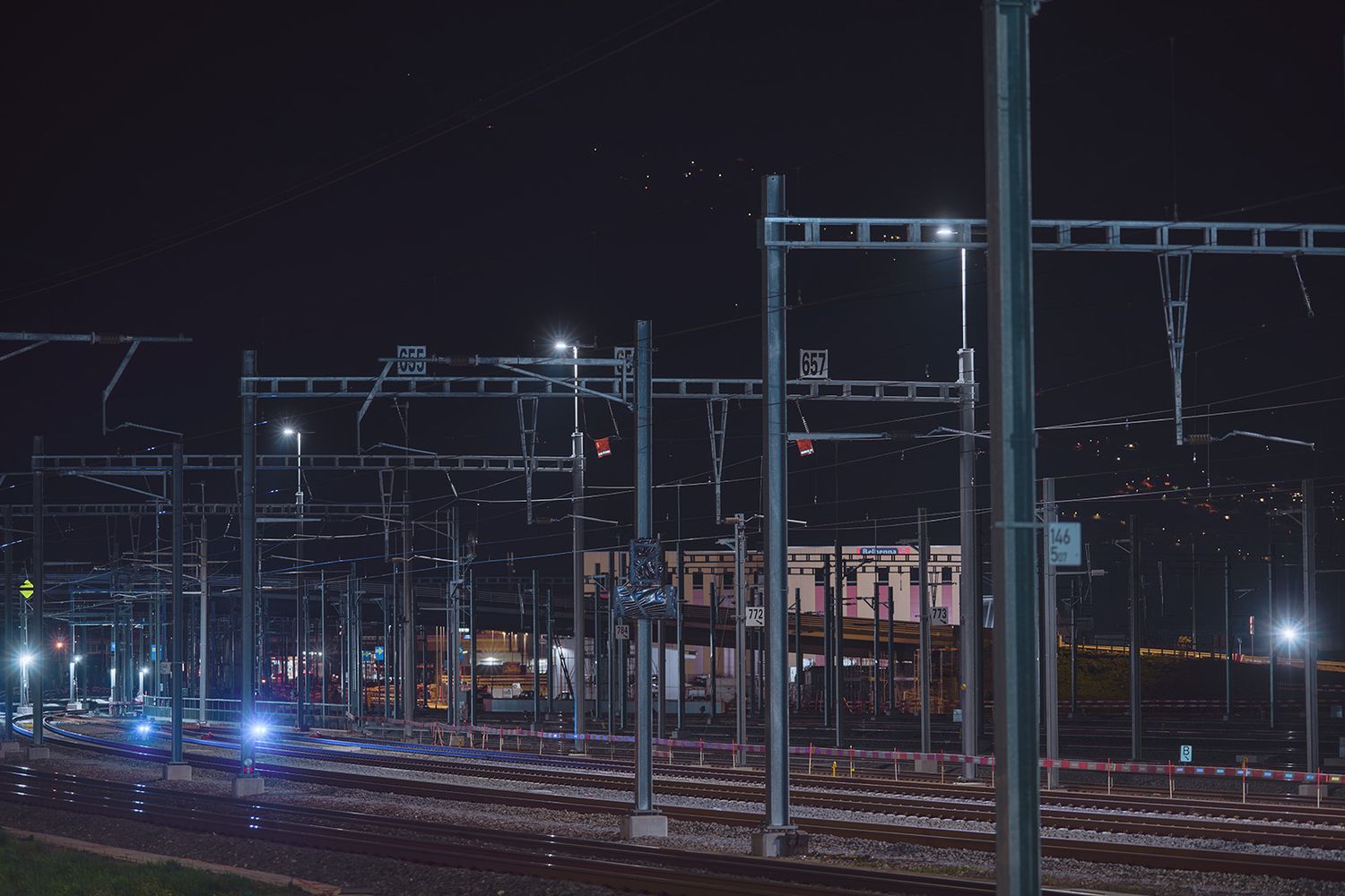 Linea ferroviaria illuminata di notte a Bellinzona con pali della catenaria e binari durante lavori operativi sul sistema ferroviario.