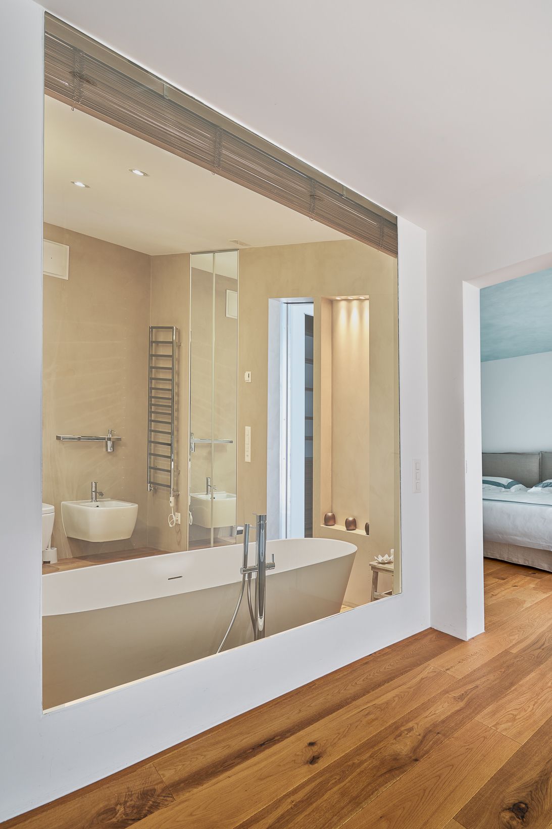 «Bagno moderno con vasca freestanding vista da ampia apertura interna, finiture chiare, dettagli in legno e scorcio della camera adiacente.»