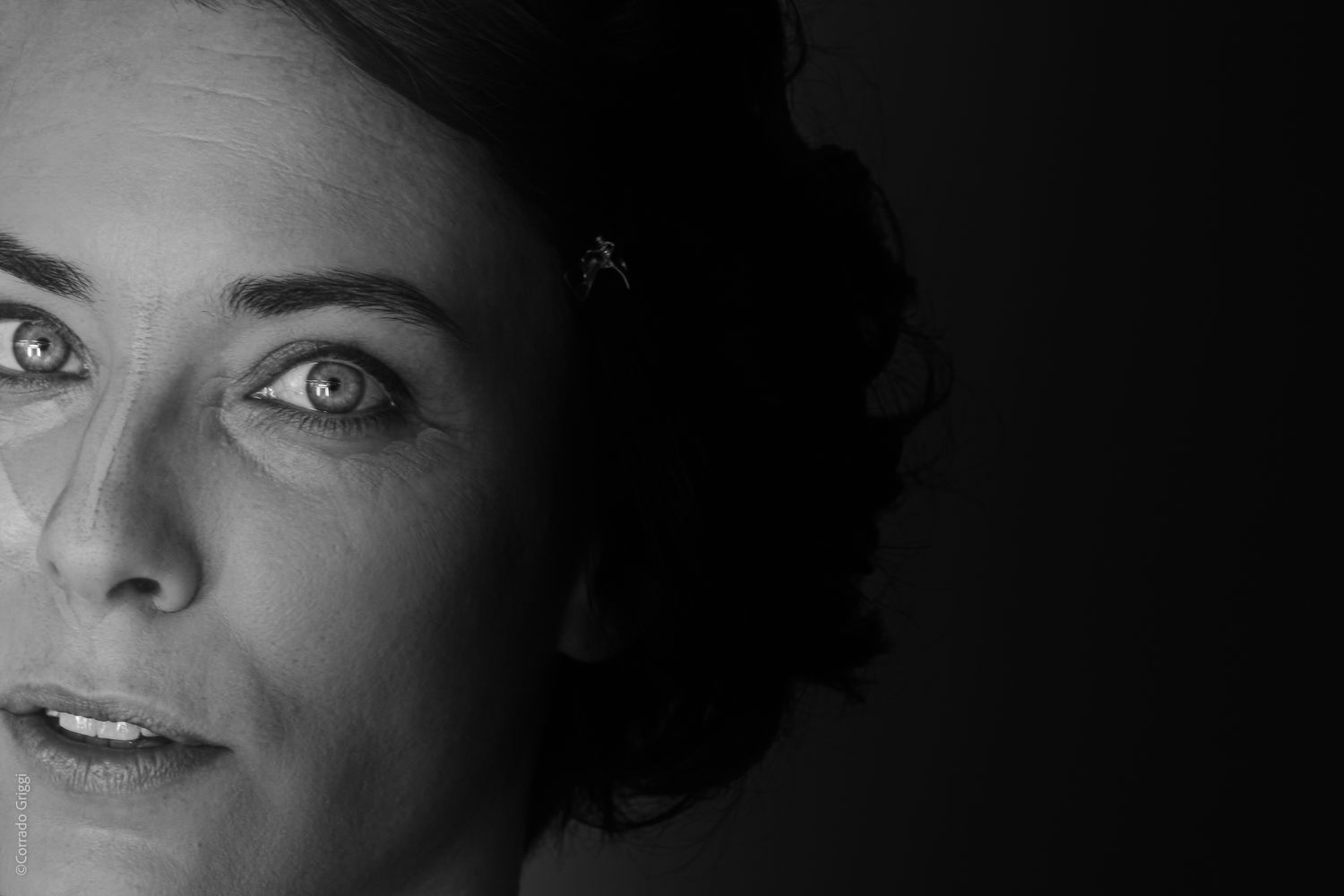 «Primissimo piano in bianco e nero, luce sugli occhi e sul volto con segni di preparazione estetica per il trucco.»