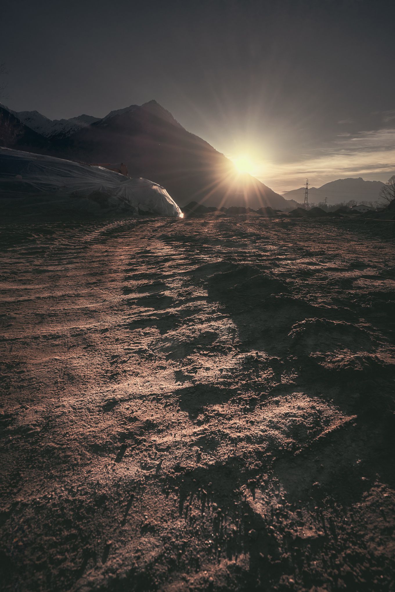 Fotografia di terreno lavorato con tracce di mezzi meccanici illuminate dalla luce radente del tramonto