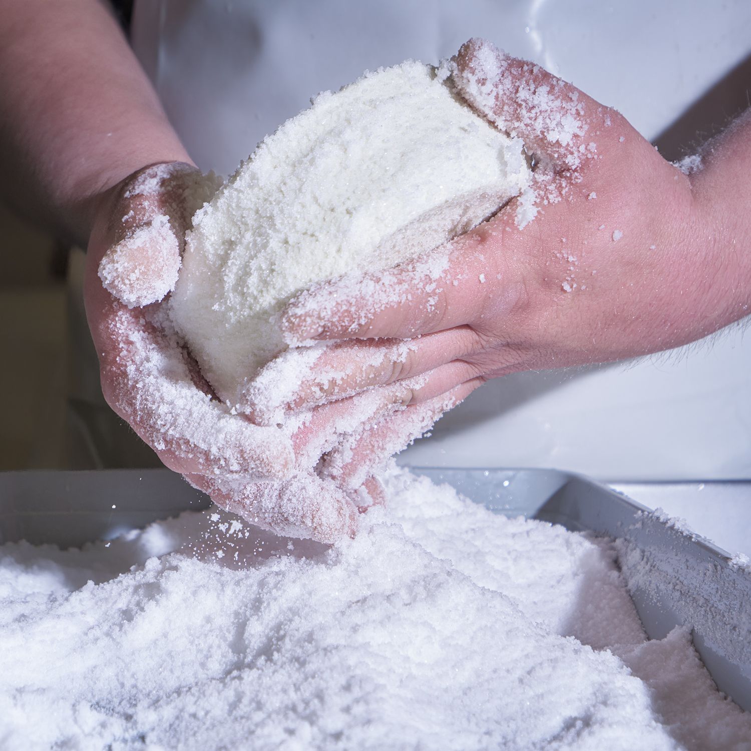 Mani che salano una forma di formaggio, luce morbida che evidenzia gesti artigianali, texture della pasta e cura del lavoro tradizionale.