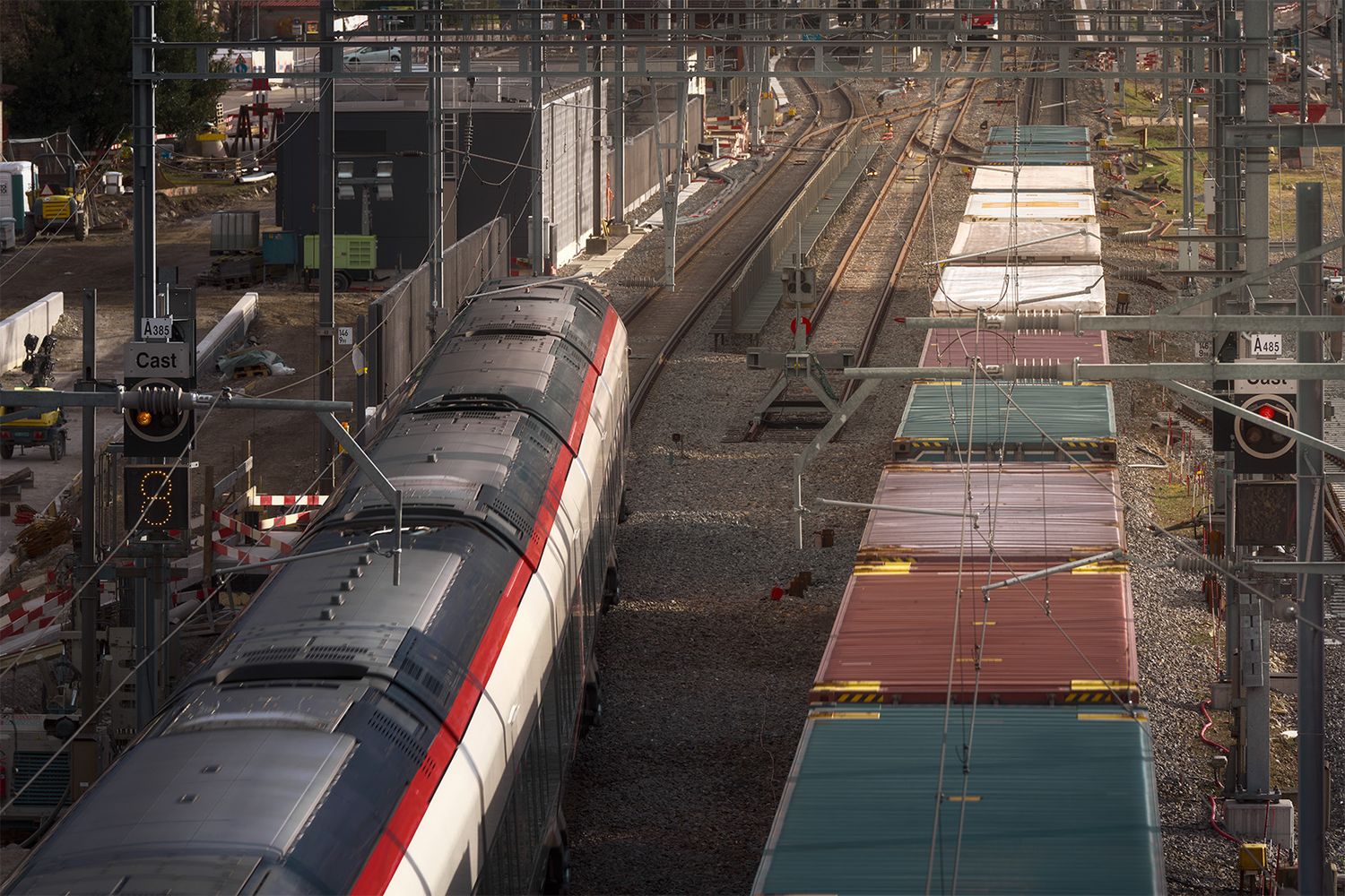 Treno in transito tra i binari nel cantiere ferroviario con segnali, linea aerea e infrastruttura ferroviaria operativa.