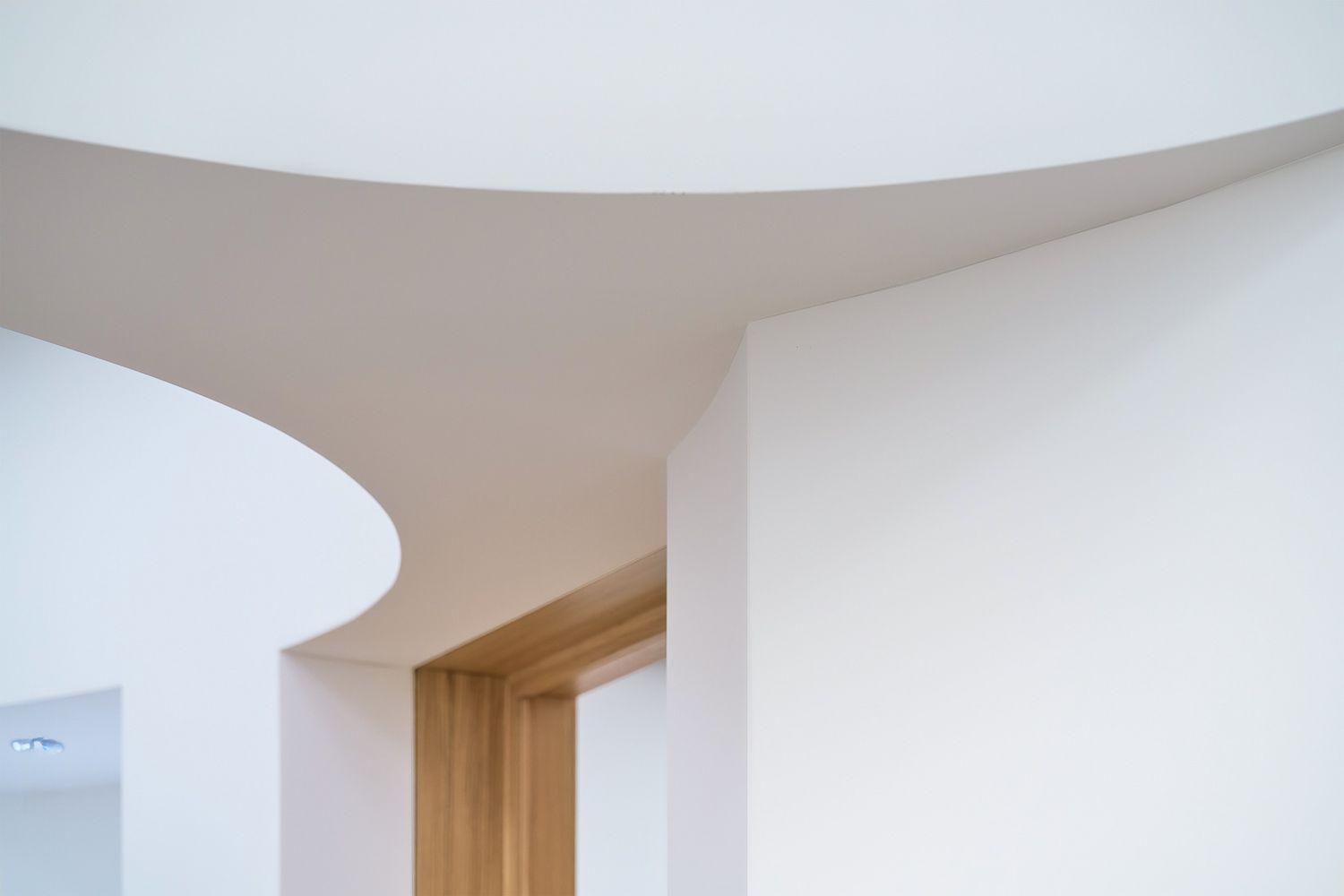 Dettaglio architettonico di interni moderni: curve morbide del soffitto e pareti bianche accostate a un varco in legno.