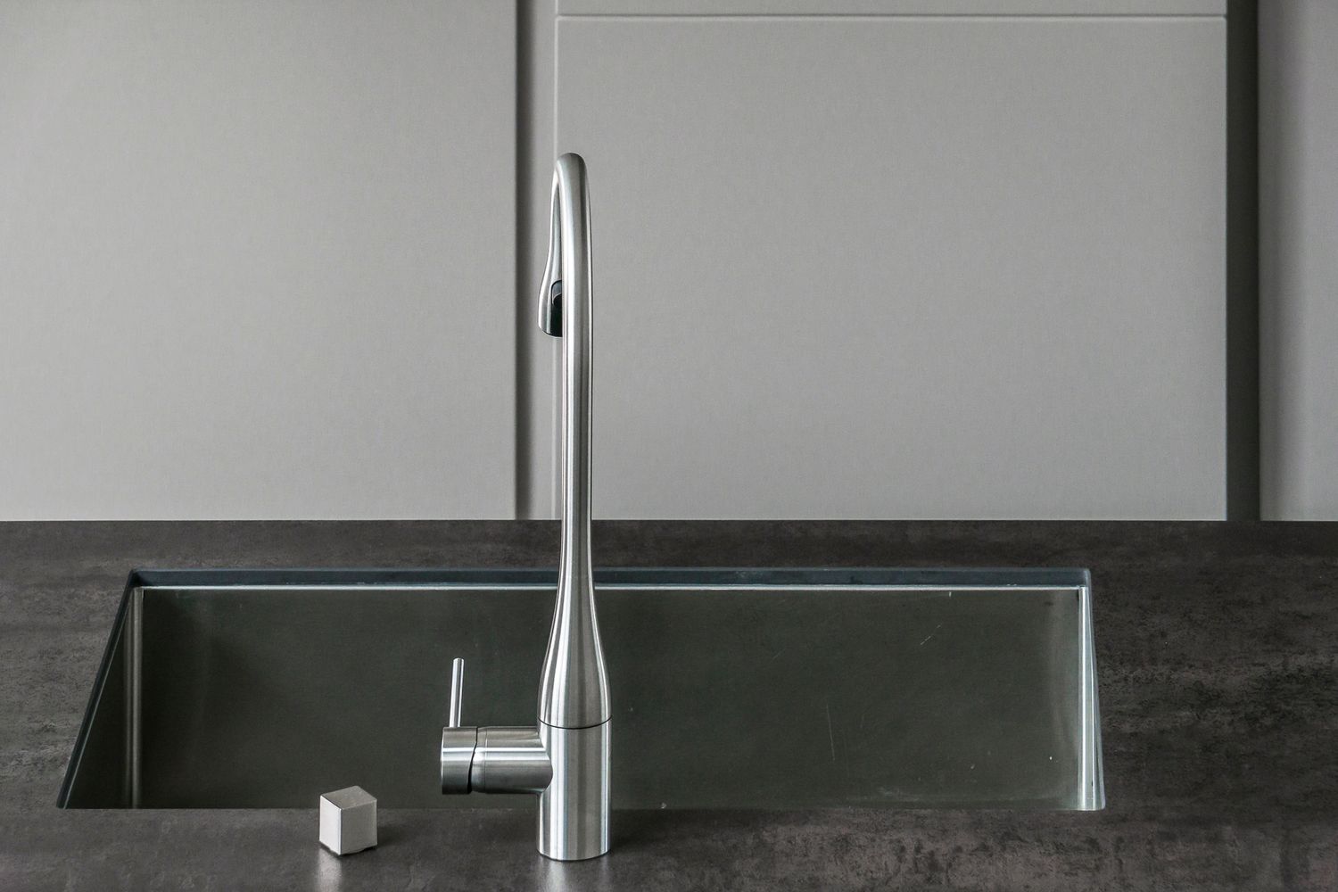 «Dettaglio di interior design: lavello a incasso con rubinetto in acciaio su piano scuro, in cucina moderna dalle linee essenziali.»