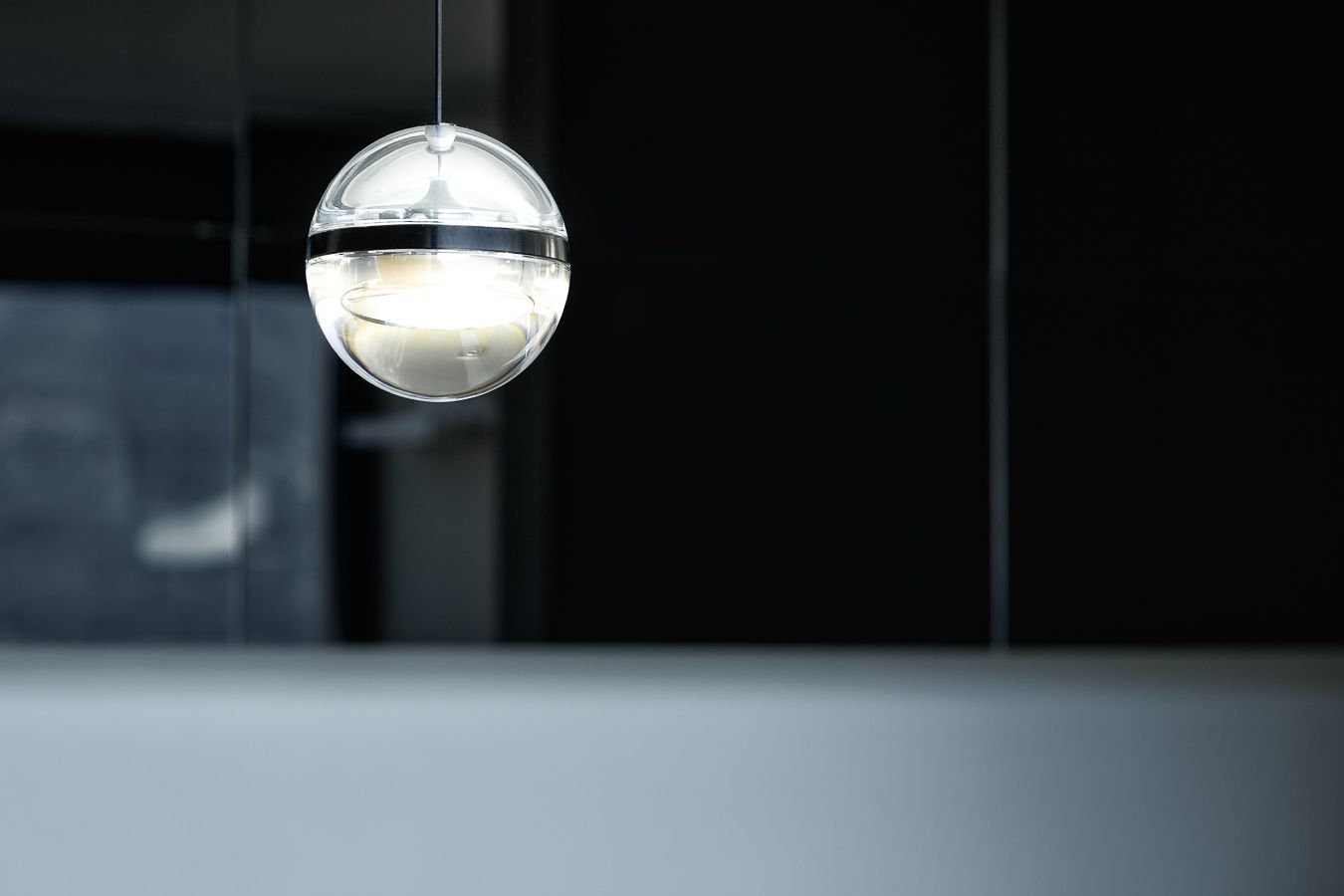 Dettaglio di interior design: lampada a sfera sospesa in vetro e metallo, illuminata su sfondo scuro in ambiente moderno.