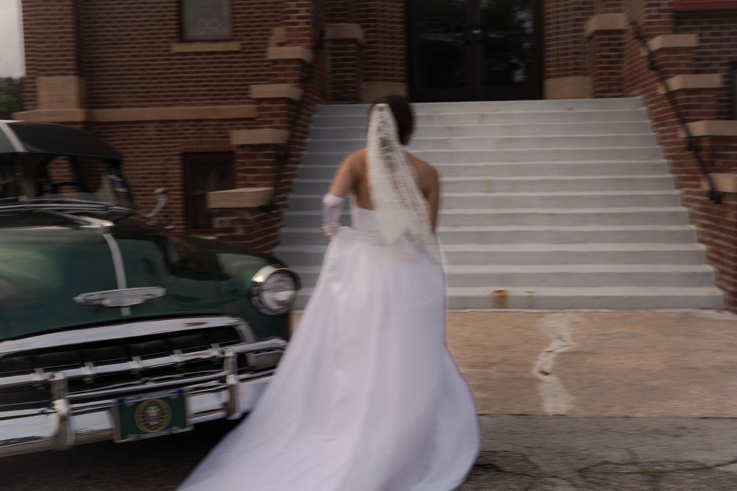 Trendy low shutter wedding shot of bride running up to chapel next to vintage car in Belle River Minnesota