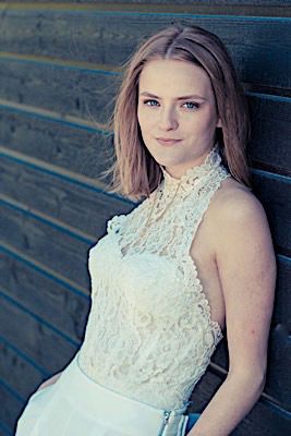 Portrait of woman in white lace halter dress against blue wooden wall.