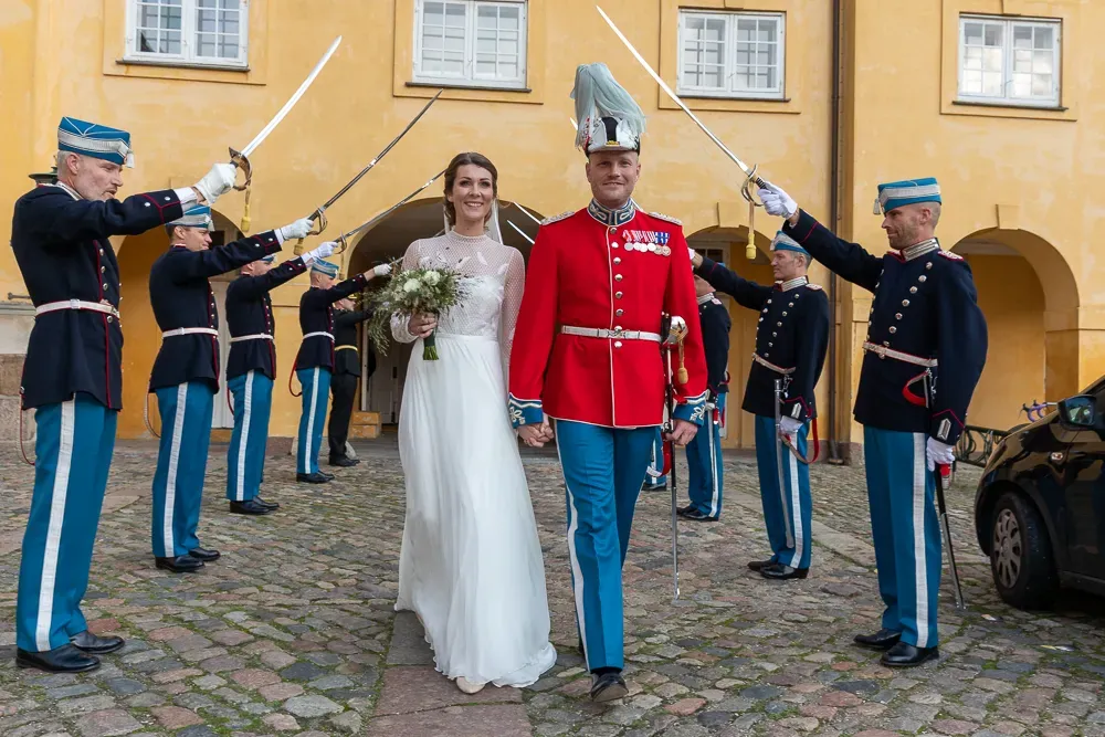 Military honor guard performs sword salute for bride and groom in formal dress.