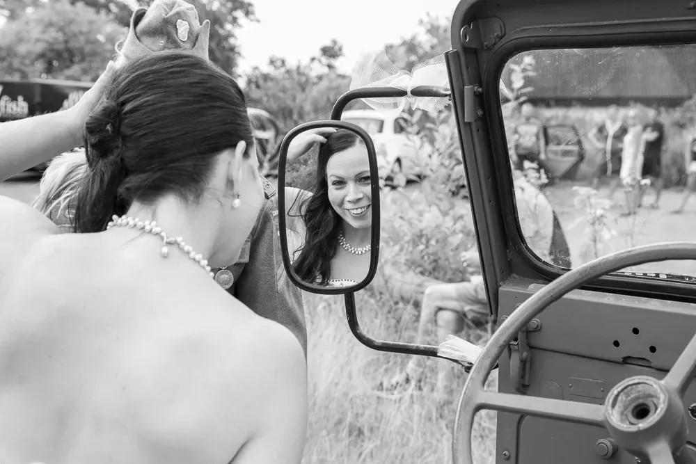Vintage black and white photo of bride checking her reflection in car mirror.