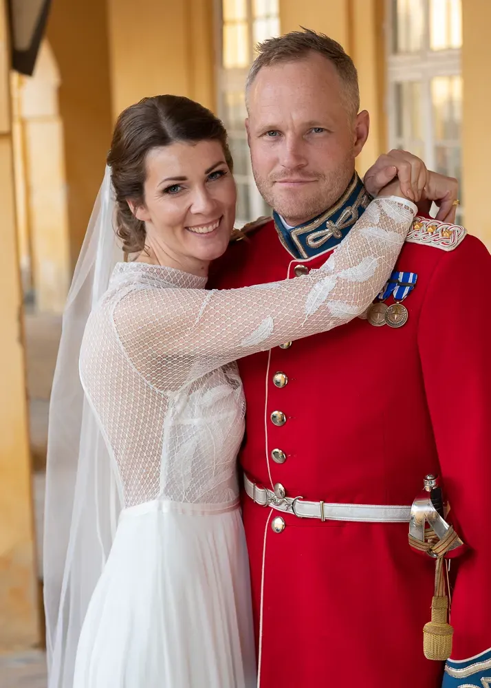 A happy wedding couple pose together, with the groom wearing a formal red military uniform.