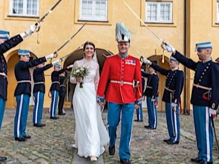 Military honor guard forms a sword arch for newlyweds outside a yellow building.