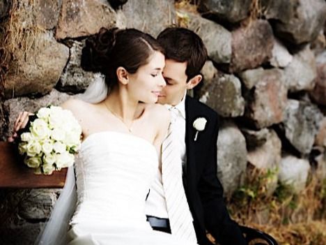 Intimate wedding portrait of newlyweds against a stone wall with white bouquet.