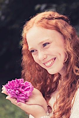 Joyful portrait holding pink flower with natural curls and white lace dress.