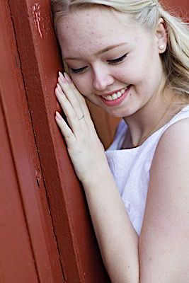 Close-up portrait against a red wall showing joyful expression and casual white top.