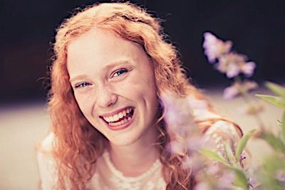 Artistic portrait with natural light showing radiant smile and soft floral elements.