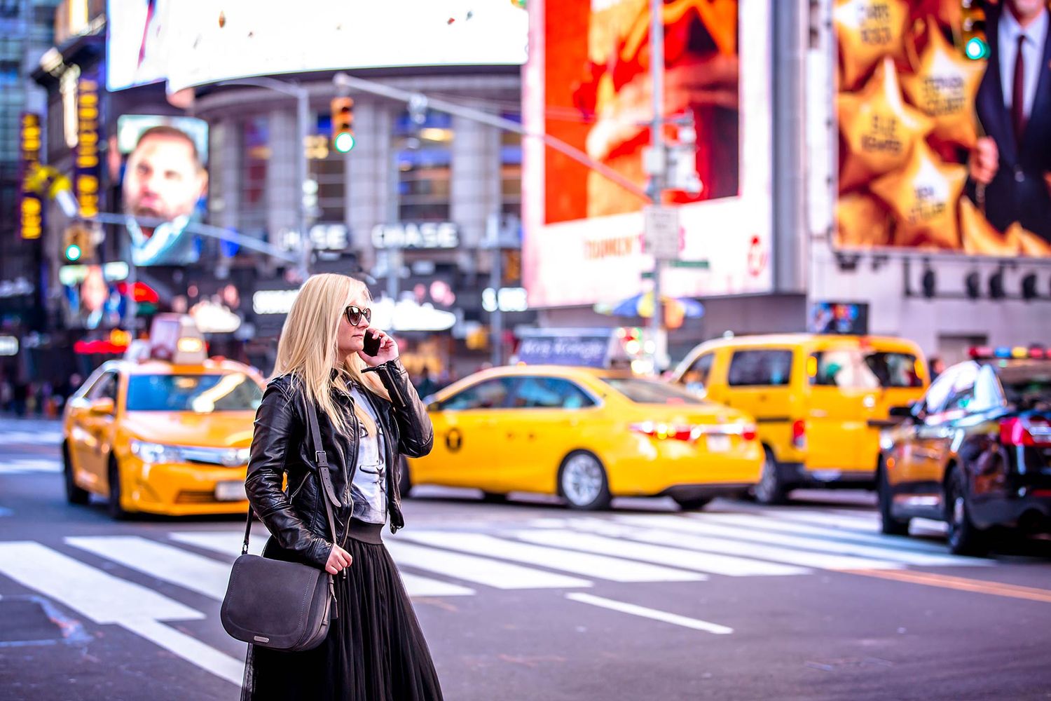 Woman in black dress takes photos near yellow taxis in Times Square, New York City.