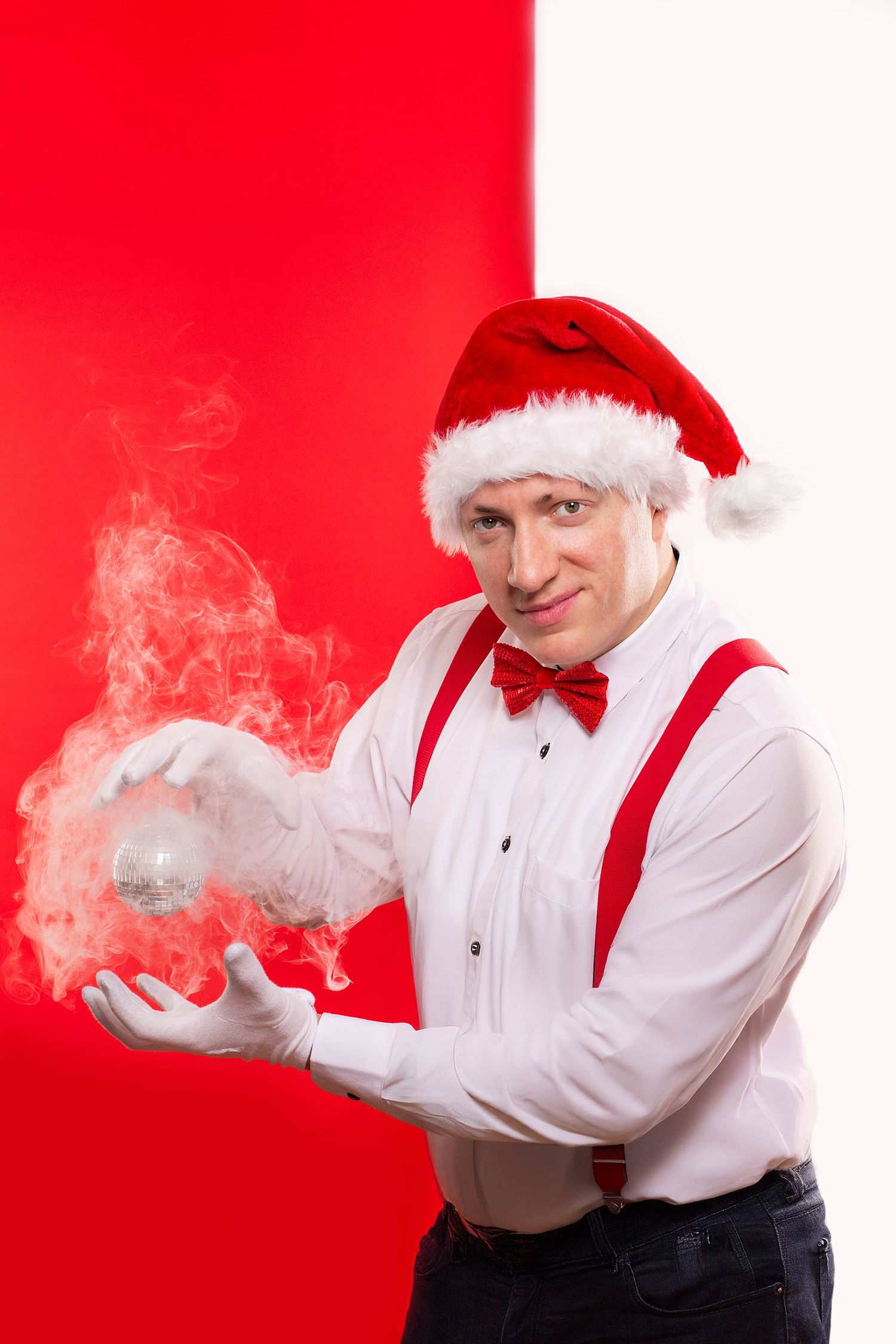 Festive portrait with suspenders and Santa hat manipulating smoke effect against red background.