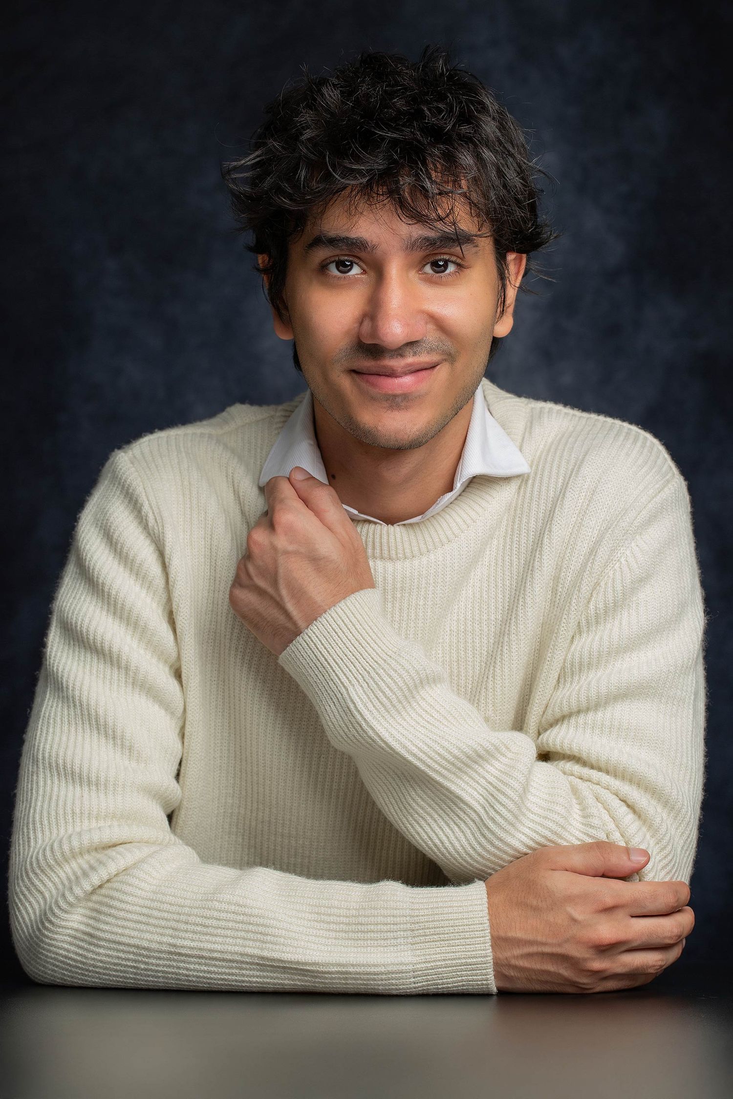 Studio portraits showing relaxed expressions in white sweater against dark backdrop.
