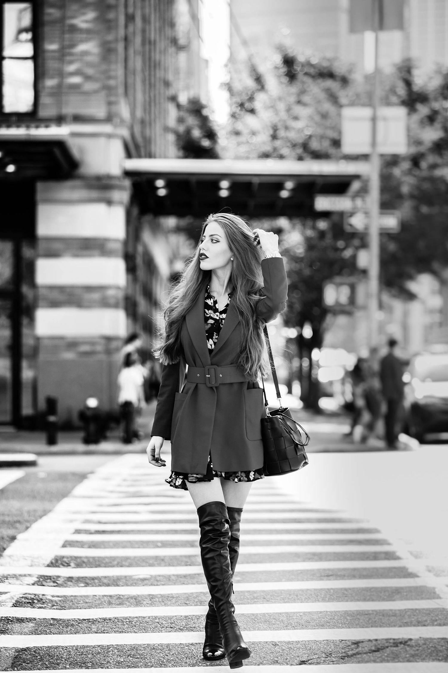 Street fashion photo of woman in black dress and boots crossing urban crosswalk.