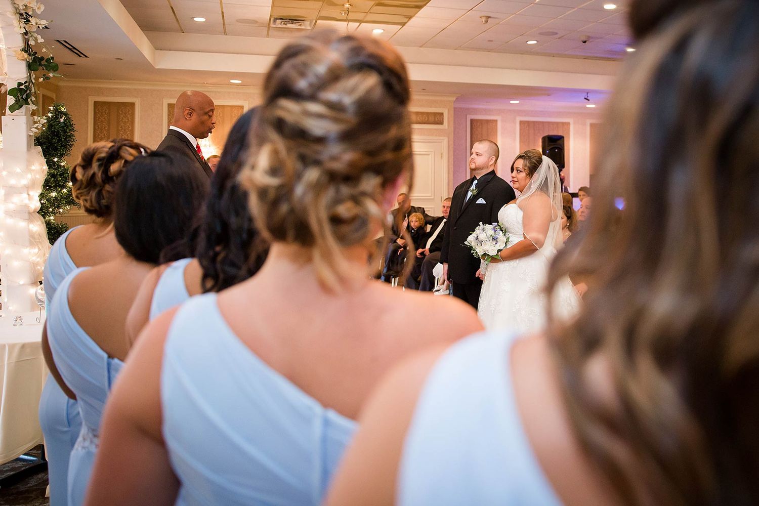 View of wedding ceremony from behind bridesmaids in light blue dresses.