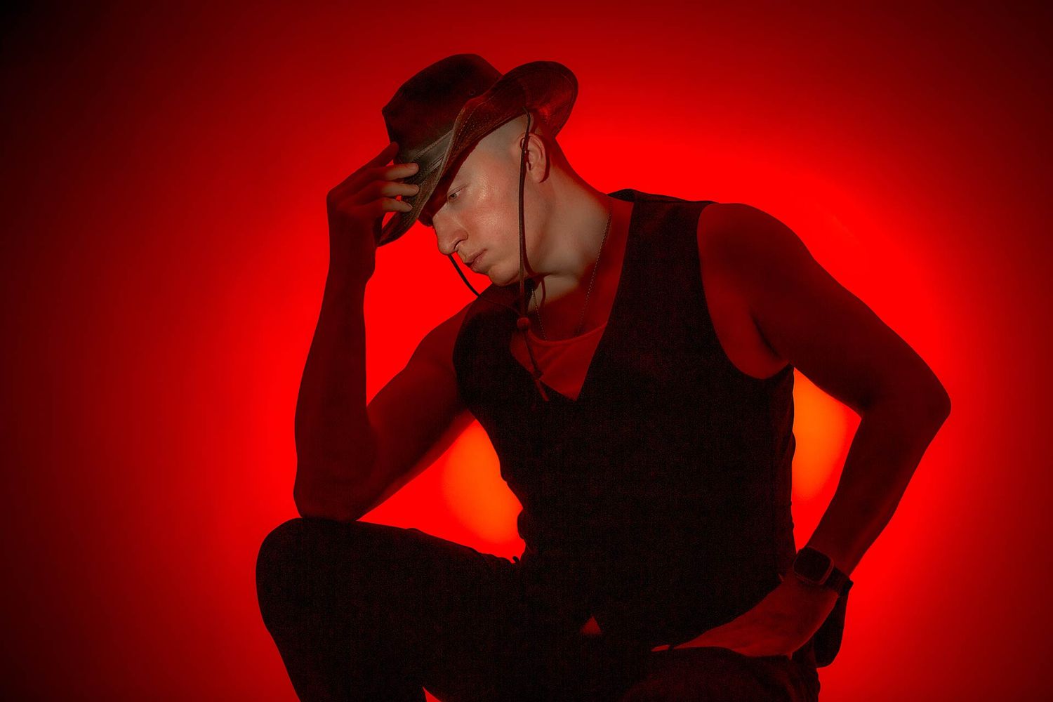 Moody artistic portrait with figure in dark clothing against intense red background lighting.
