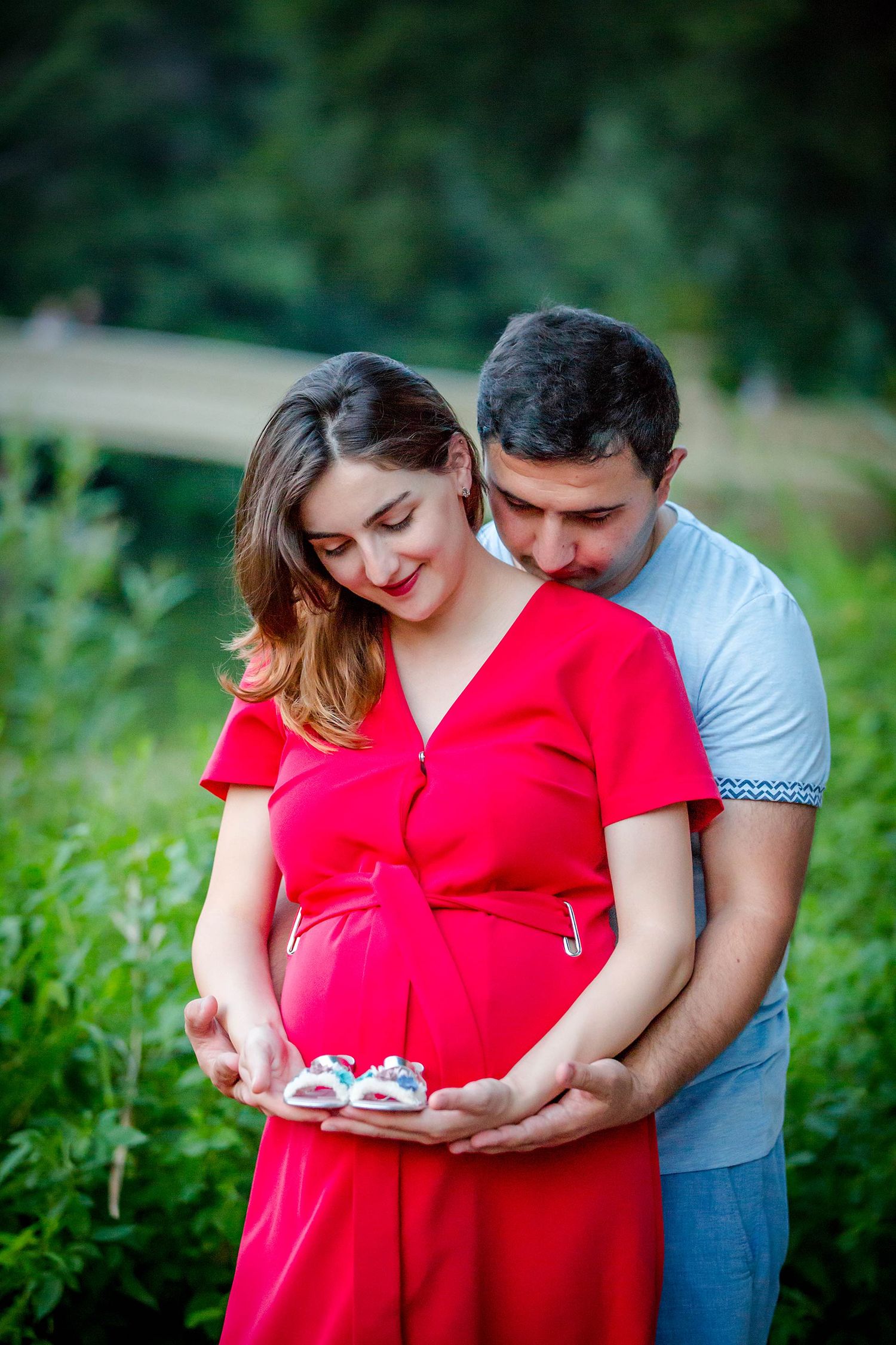 Couple in red dress and gray shirt sharing intimate moment in garden setting.