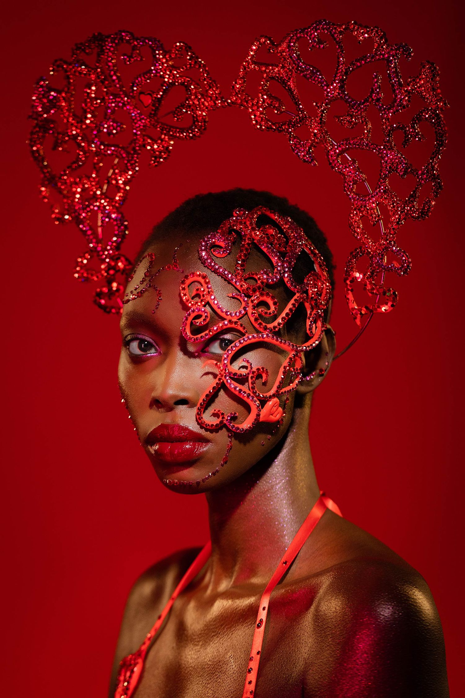 Creative beauty portrait with intricate red lace heart design against deep red background.