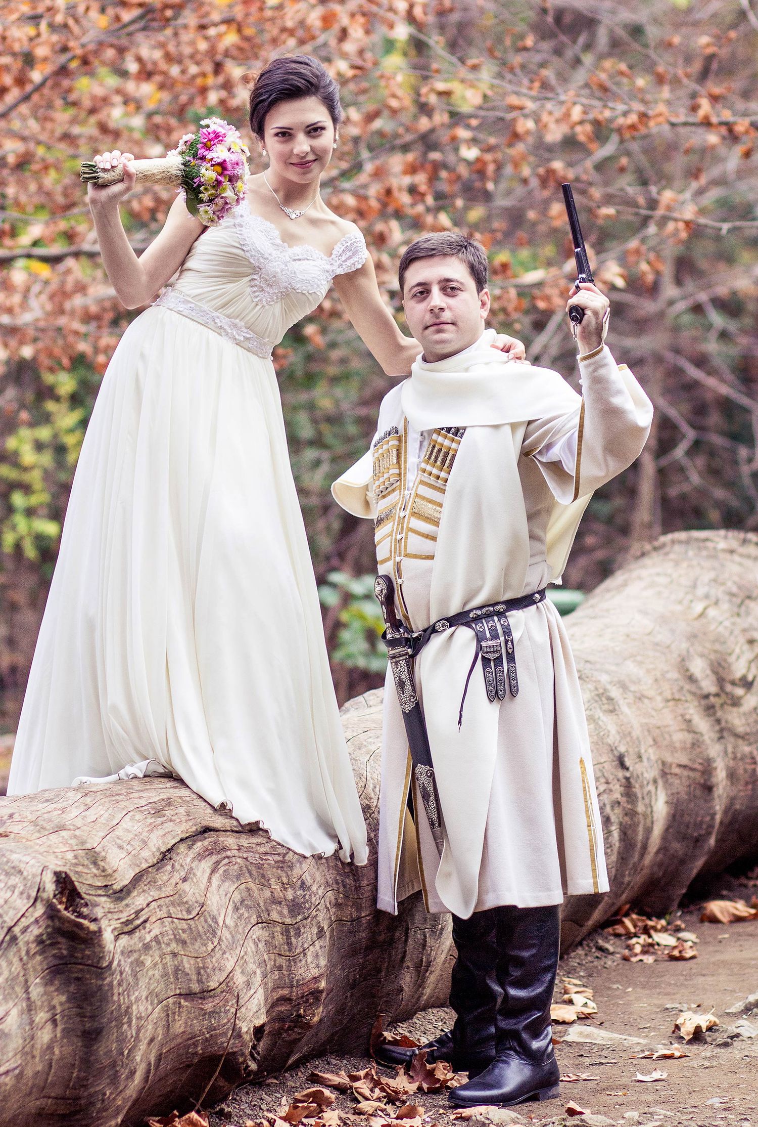 A medieval-themed couple poses on a fallen log with flowers and historical props.