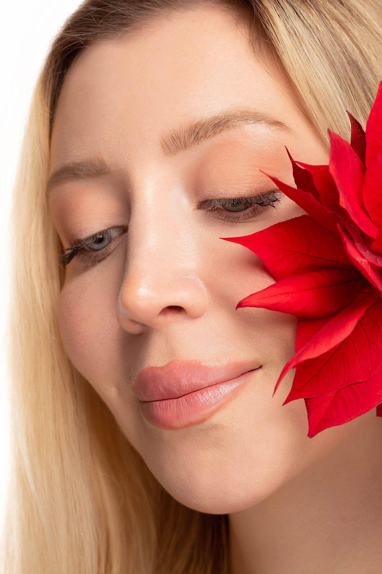Serene beauty portrait with closed eyes and red flower accent against light background.