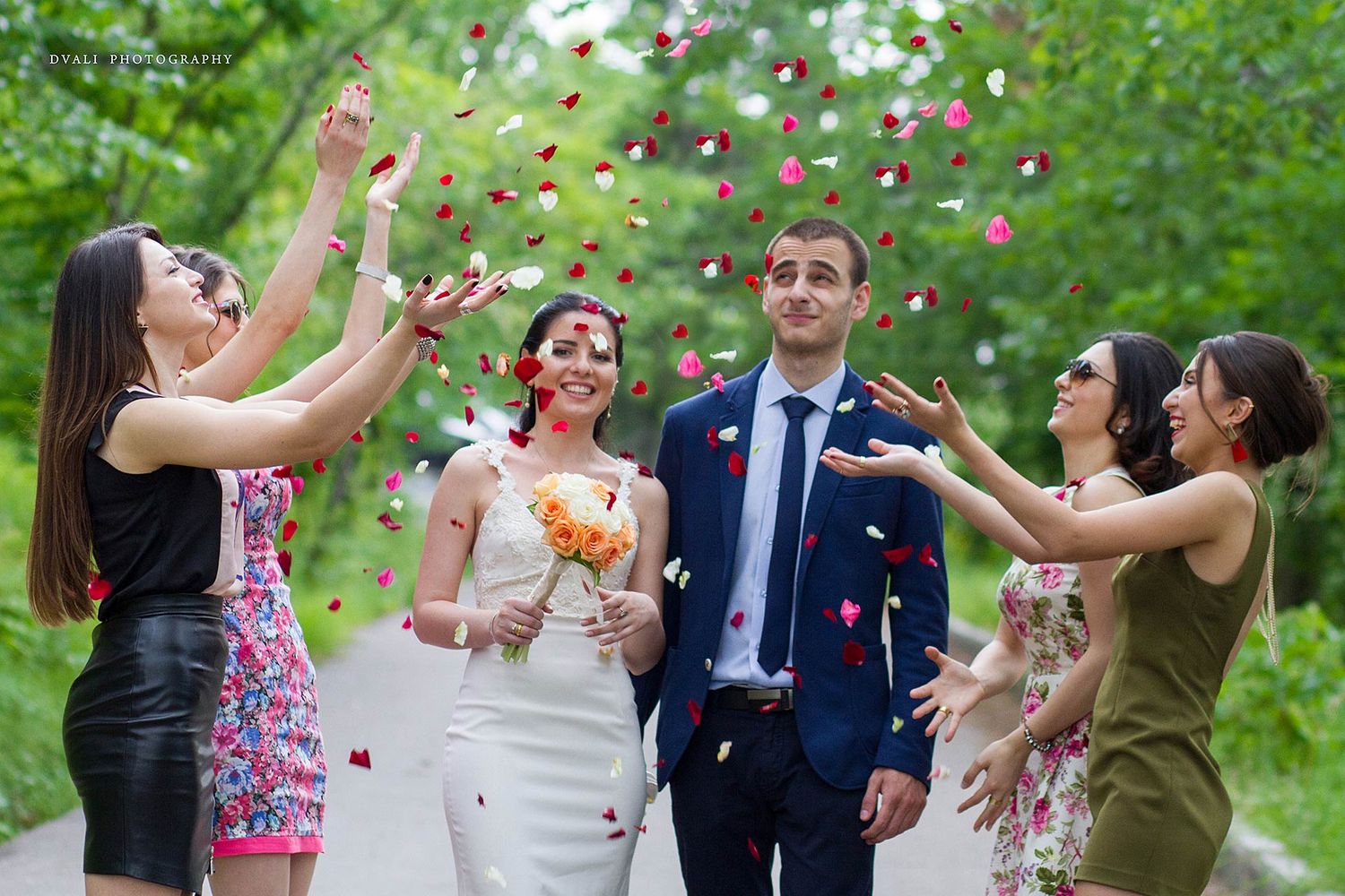 Wedding guests toss colorful flower petals during an outdoor celebration.