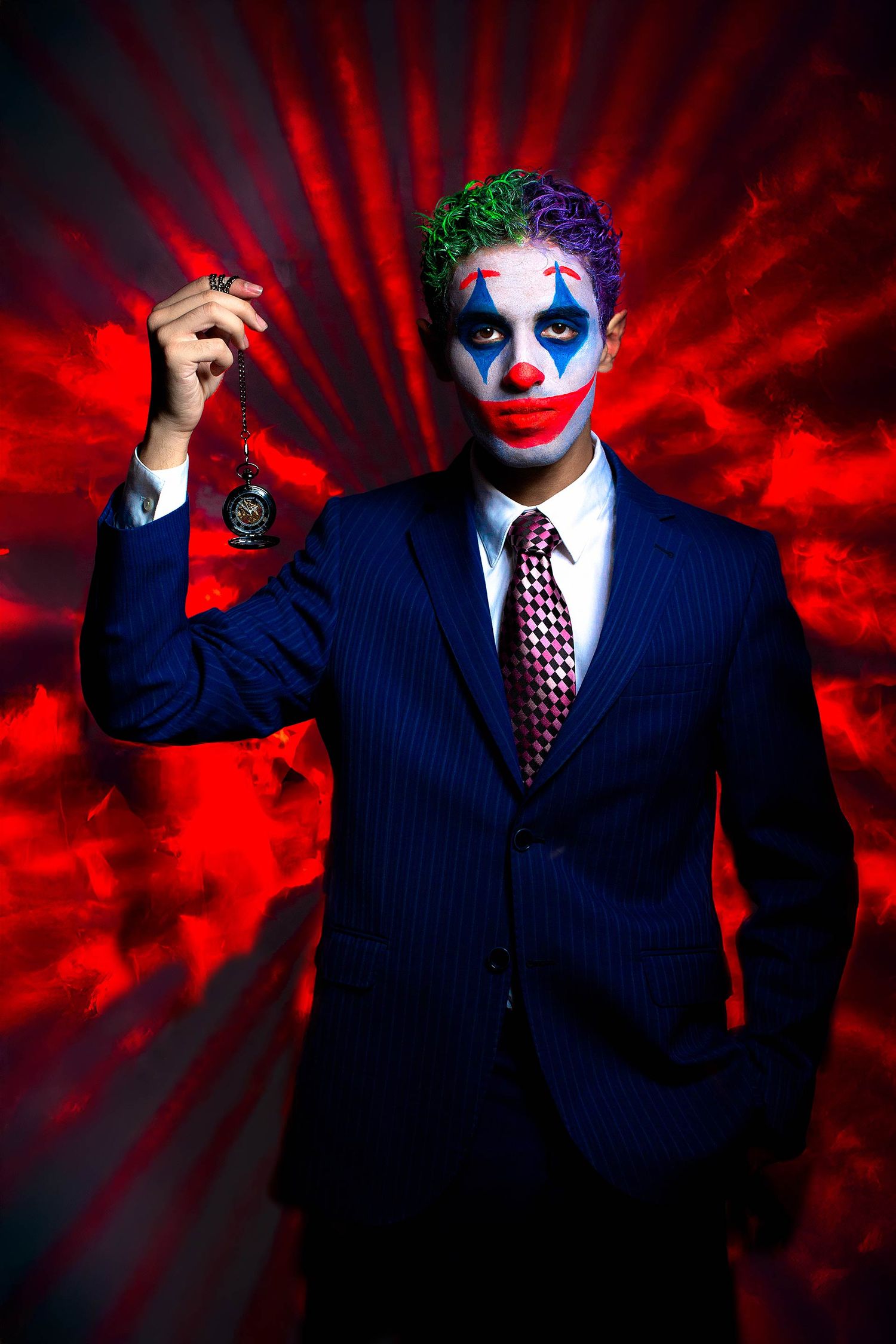 Figure in a business suit and clown makeup poses dramatically against a red background.
