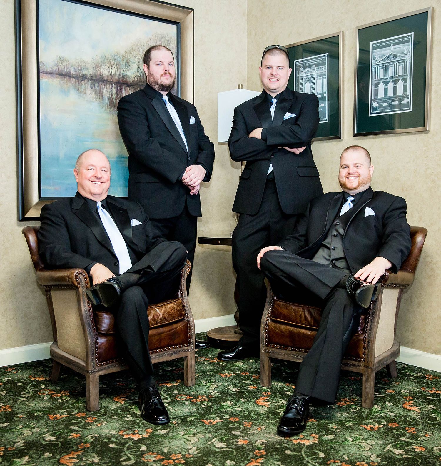 Group in black tie formalwear posed in leather chairs against decorated wall with artwork.