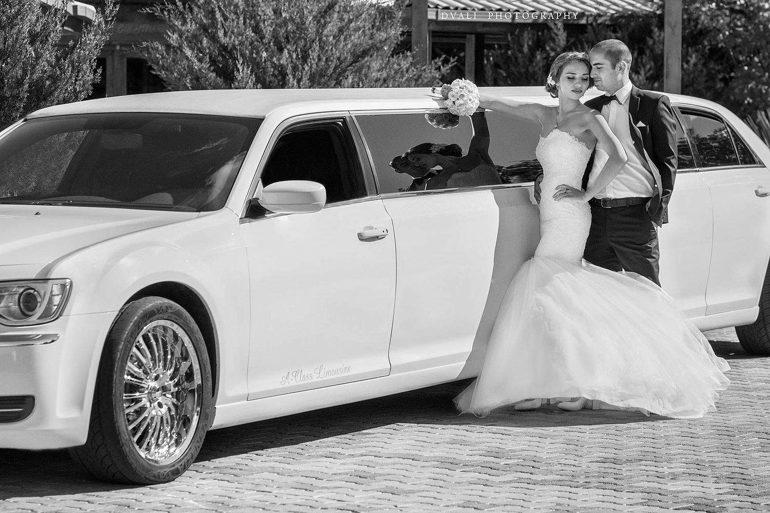 A celebratory wedding pose next to a white luxury car in black and white photography.