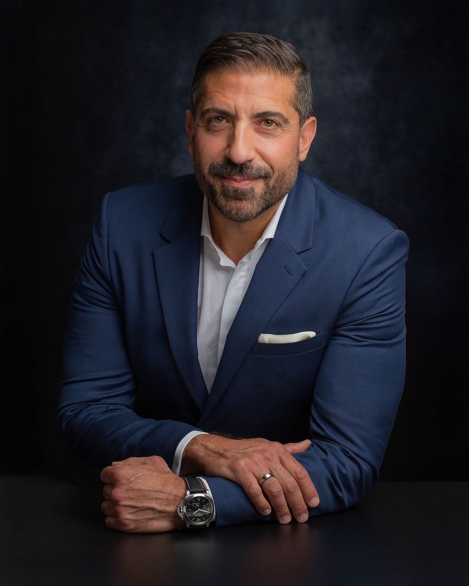 Professional headshot series of a person in a navy suit and white shirt against a dark background.
